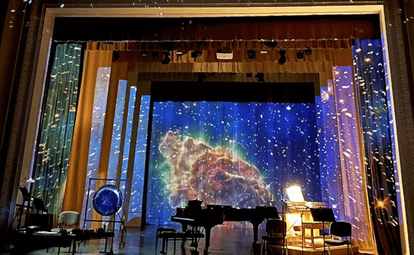 An empty stage with various instruments. A video of outer space is projected onto the stage.