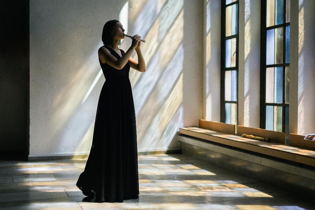 Die Musikerin in einem schwarzen Abendkleid mit Flöte in einem lichtdurchfluteten Raum mit bunten Glasfenstern