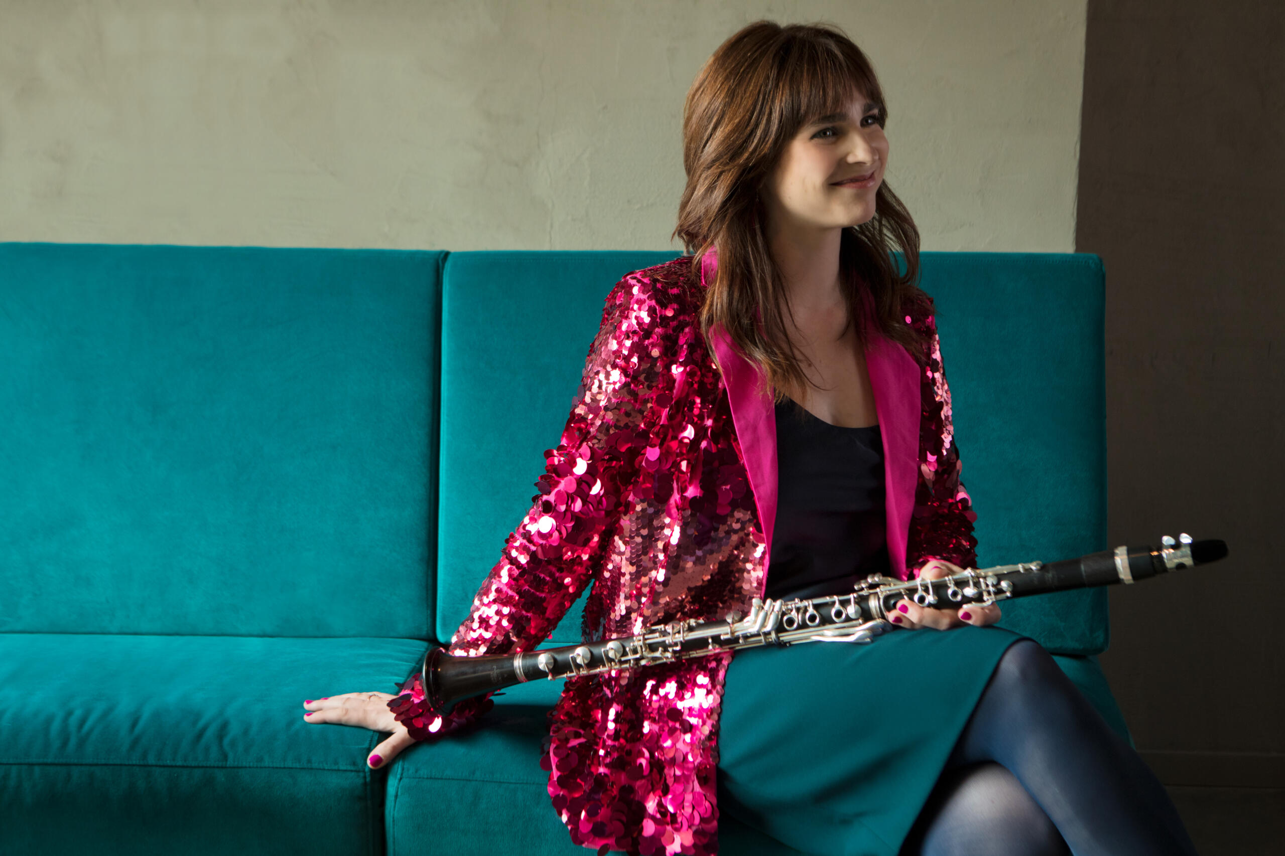 A young woman sits on a sofa with her clarinet in her hand.
