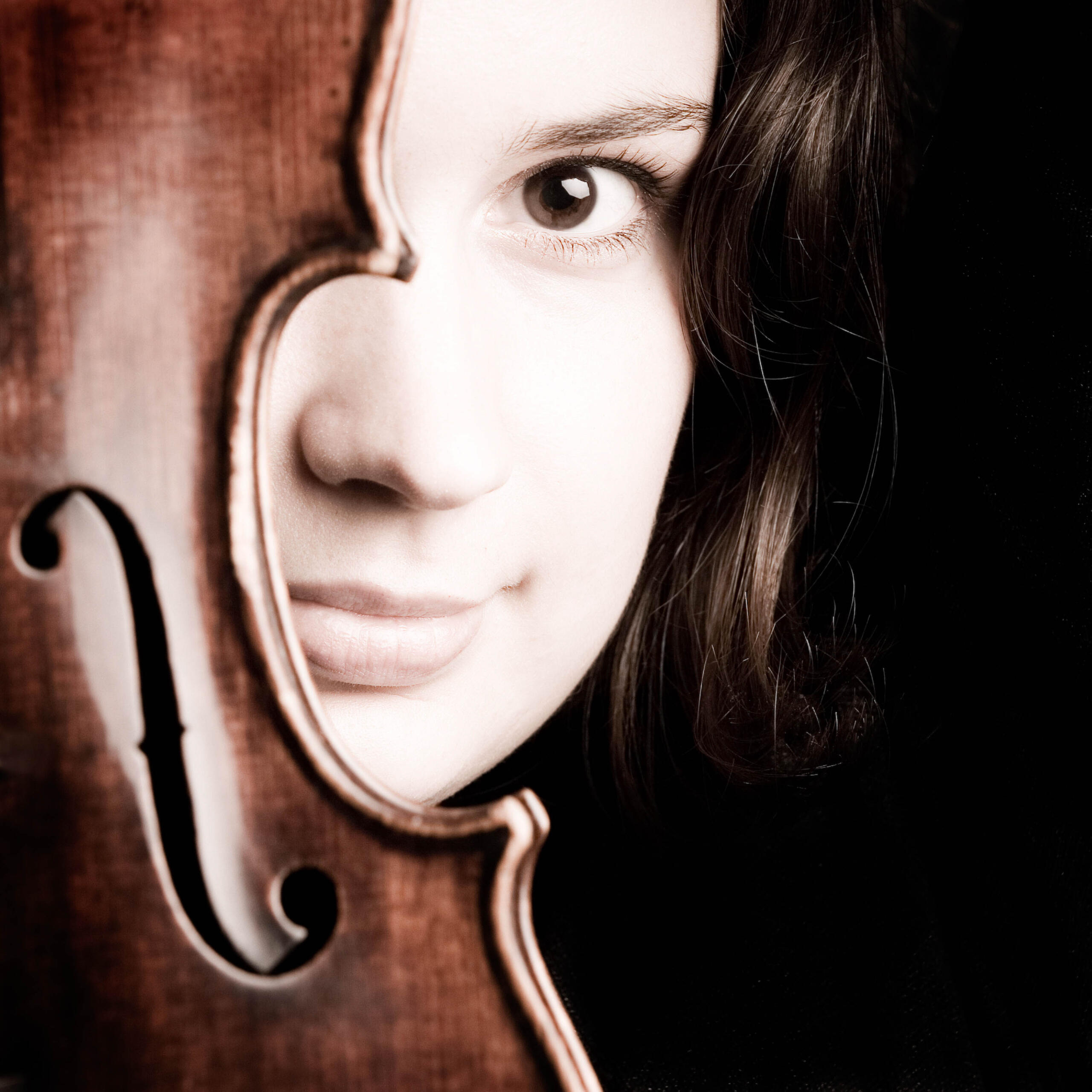Close-up of violinist Kopatchinskaja's face, half of her face is covered by a violin.