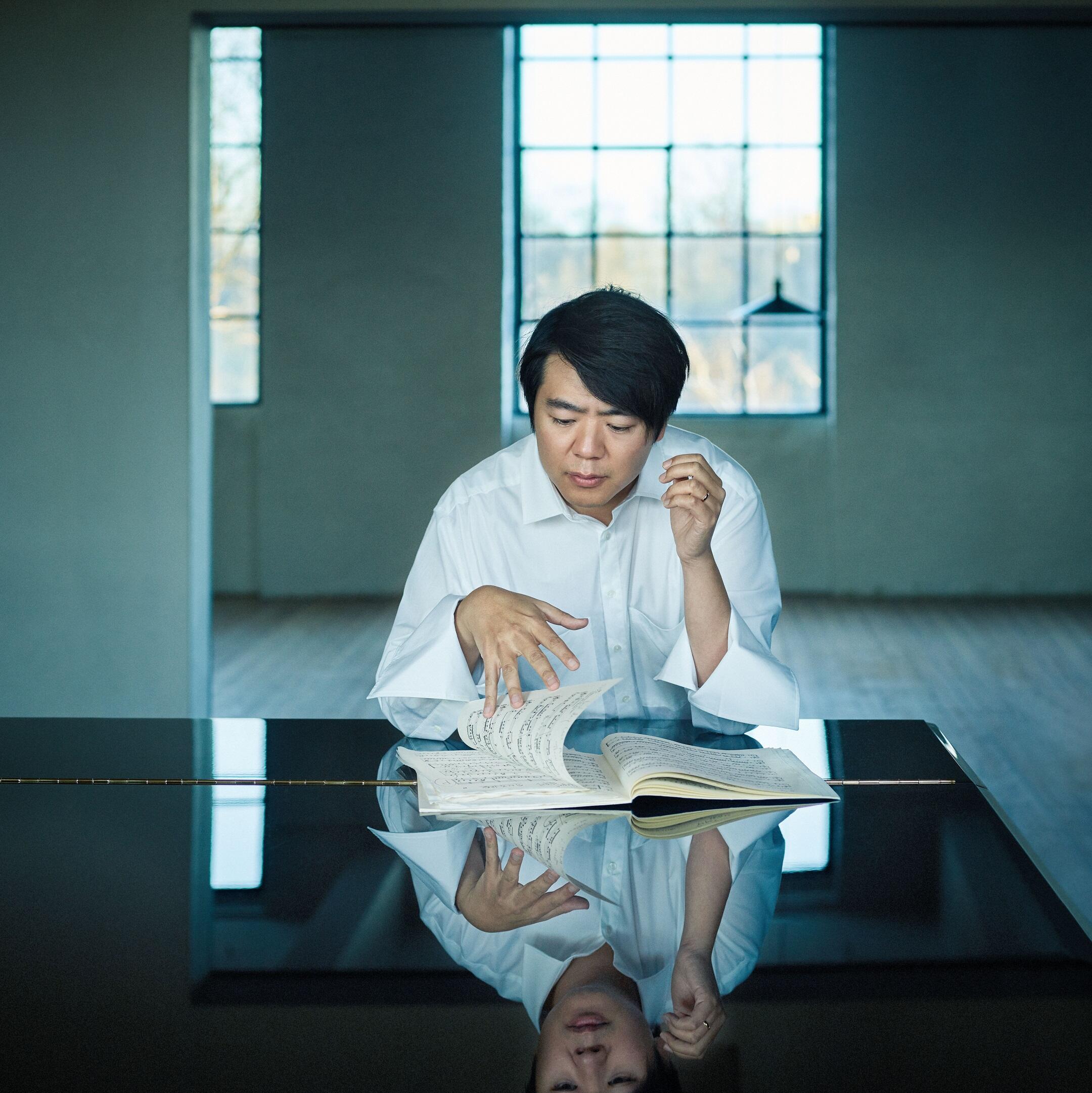 Portrait of the pianist Lang Lang. He is sitting in a bright room at a grand piano, leafing through a music book, lost in thought.