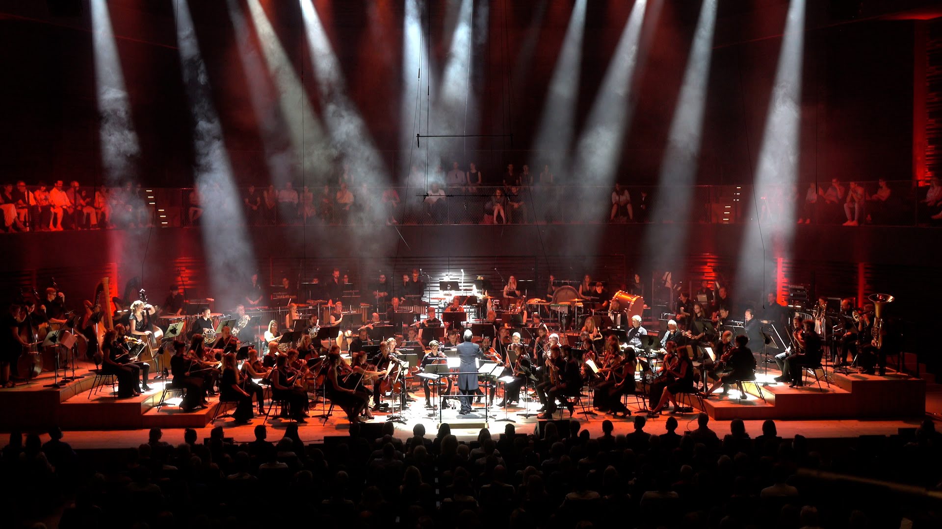 Eine Bühne im Schweiferwerferlicht mit Orchester und Dirigenten.