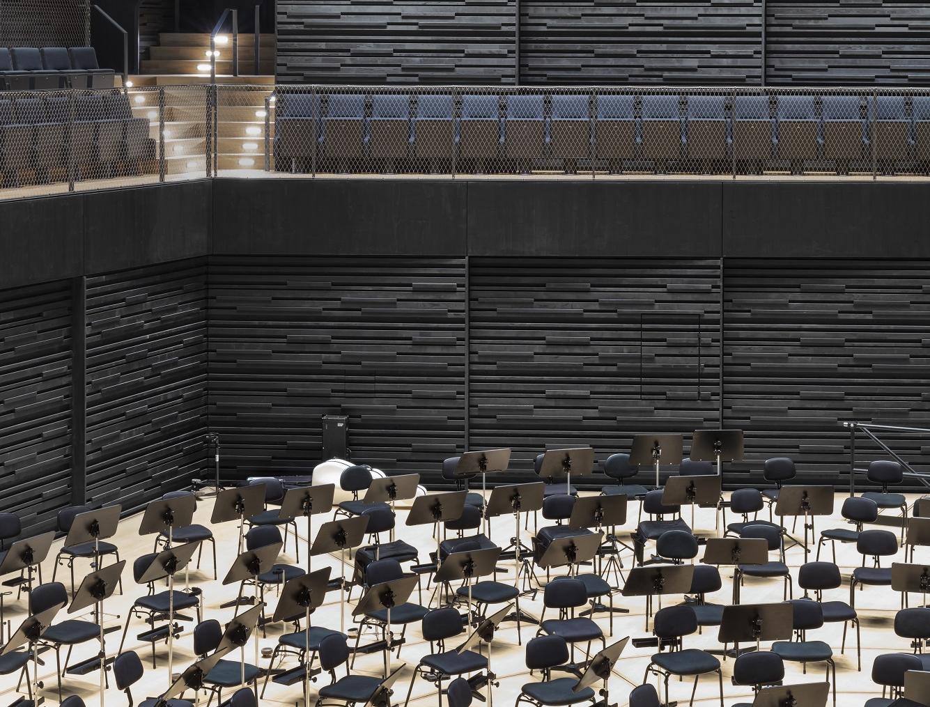 Schwarze Holzwand der Isarphilharmonie, leere Orchesterbestuhlung auf der Bühne