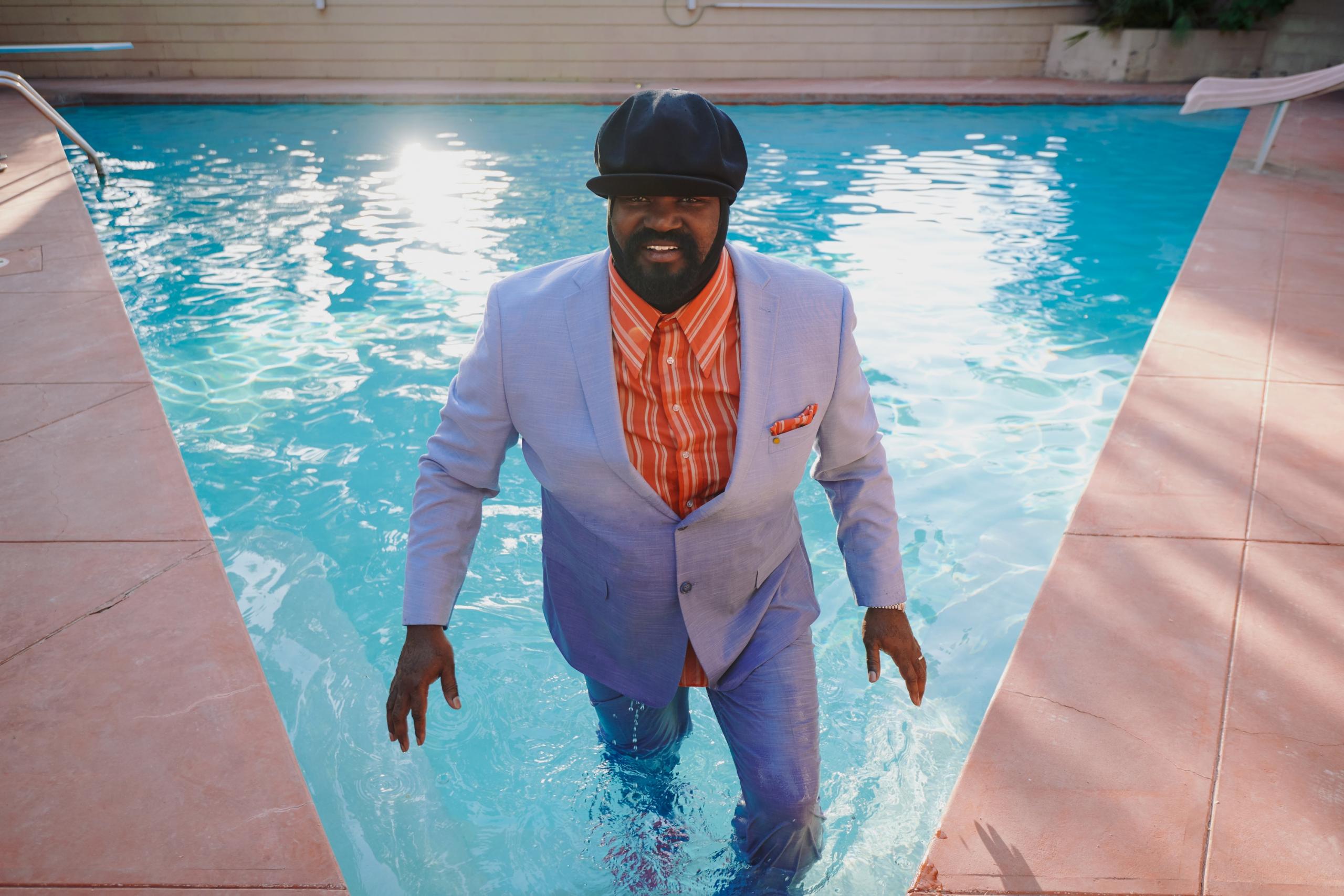 The artist stands in a suit up to his knees in a swimming pool.