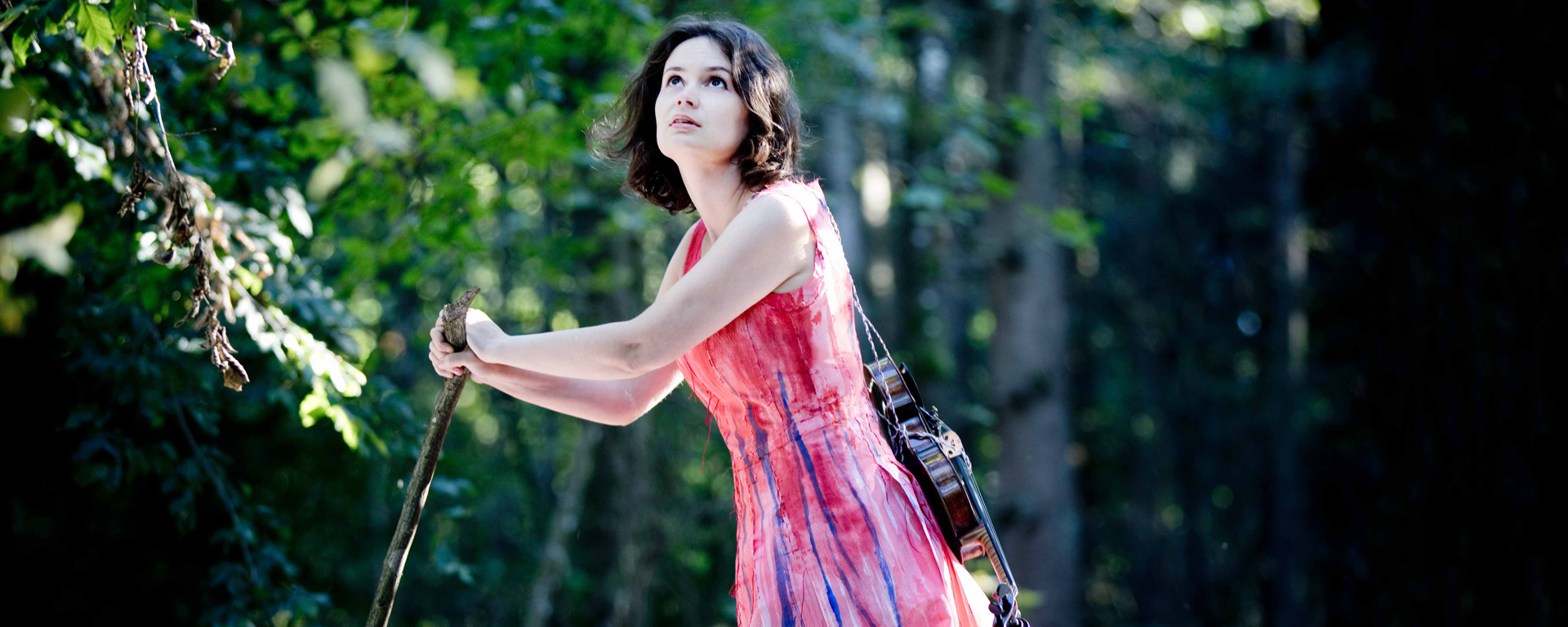 Patricia Kopatchinskaja im Wald. Die Geige trägt sie mit einer Kordel befestigt auf dem Rücken.