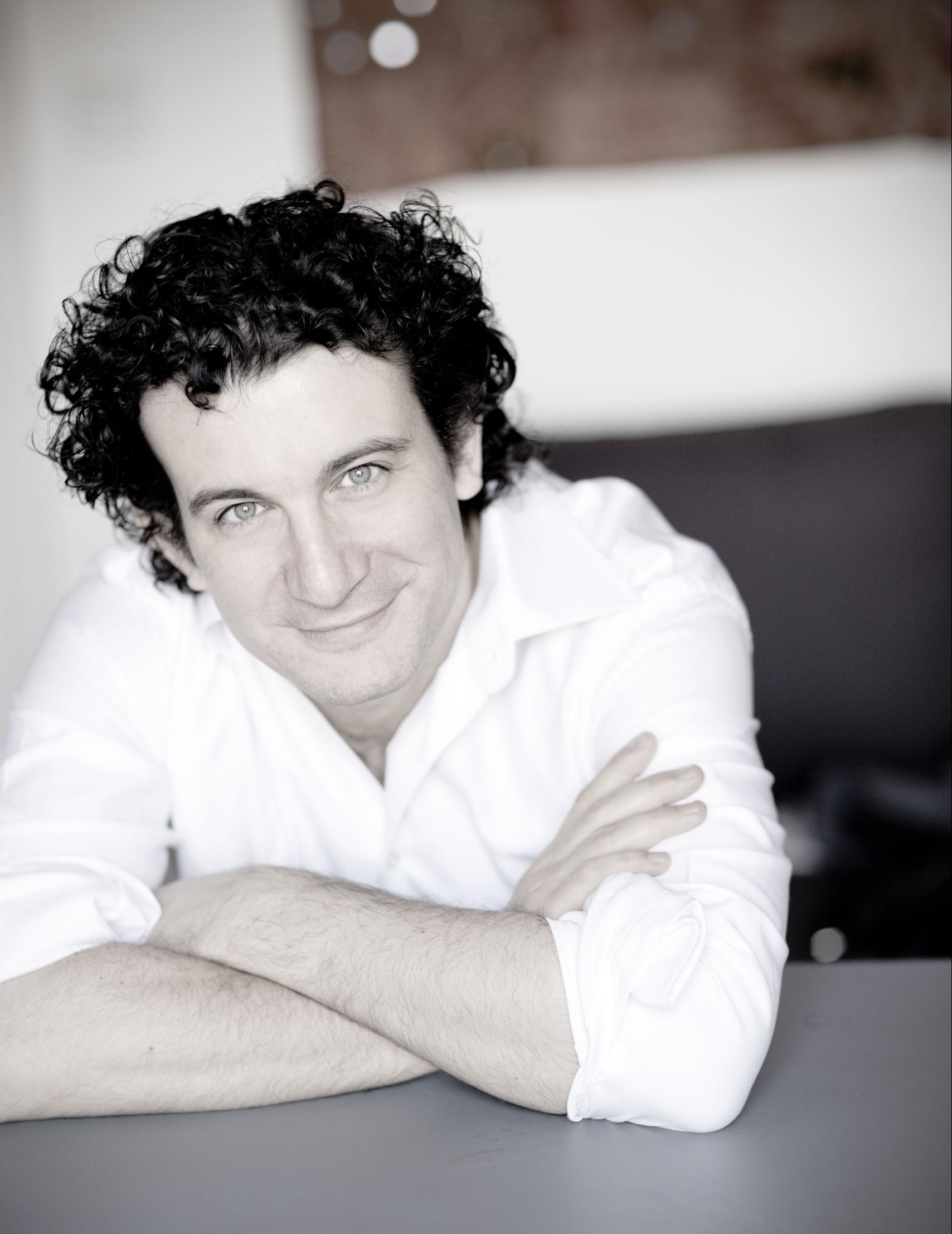 Conductor Alain Altinoglu leans with his arms on a table and smiles into the camera