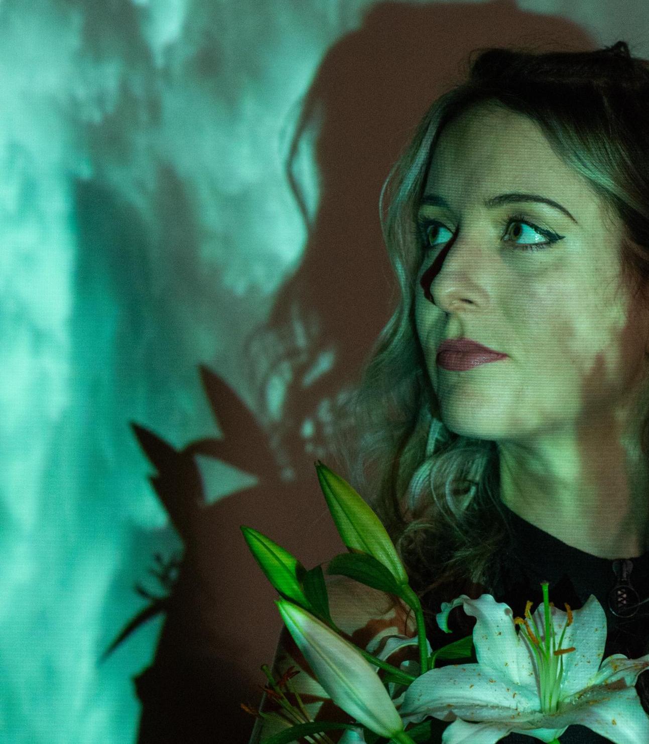 Profilporträt der DJane Alicea vor einer grün illuminierten Wand. In der Hand hält sie eine Lilie.