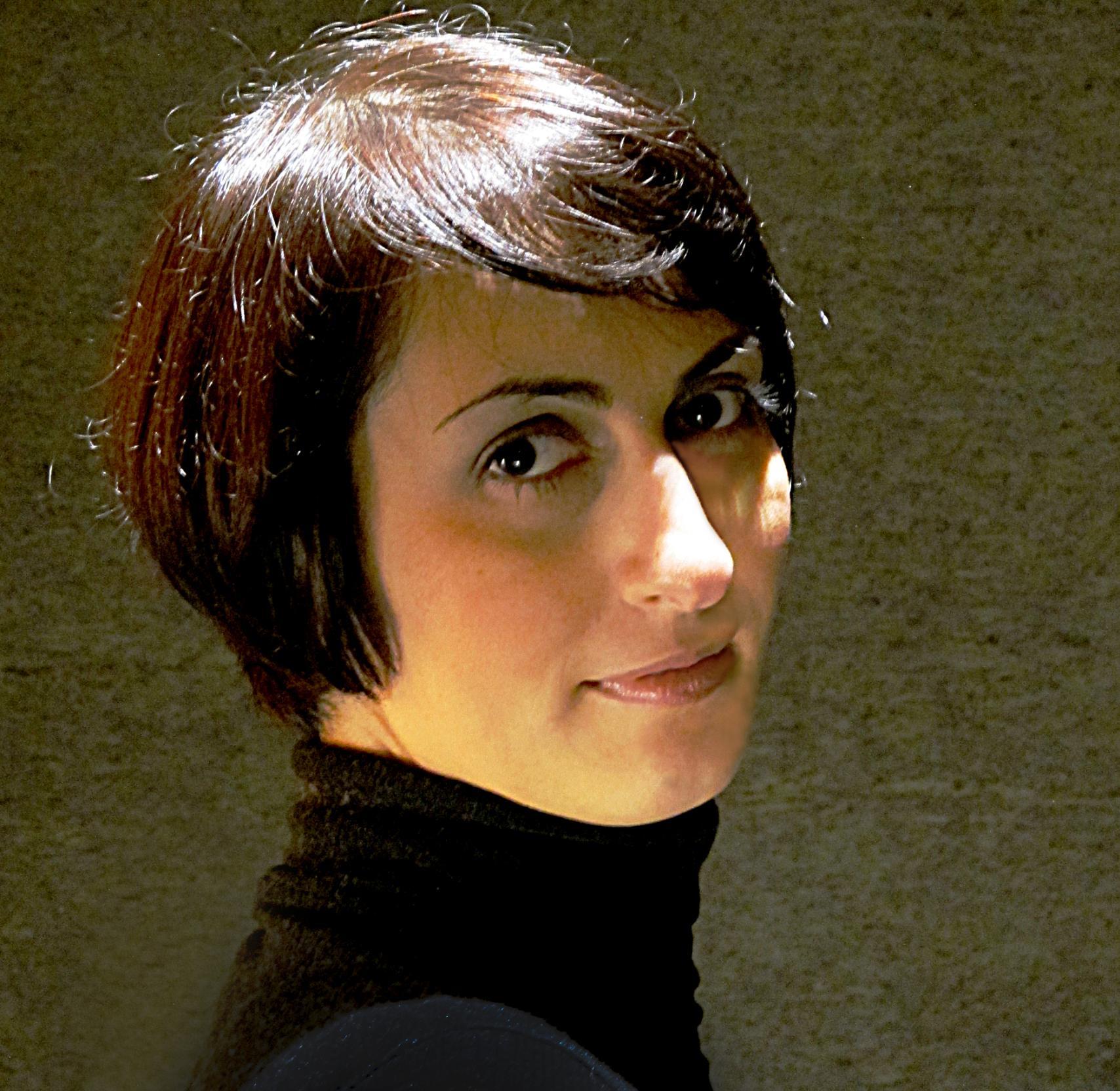 A woman in a black turtleneck sweater and with dark short hair looks at the camera.