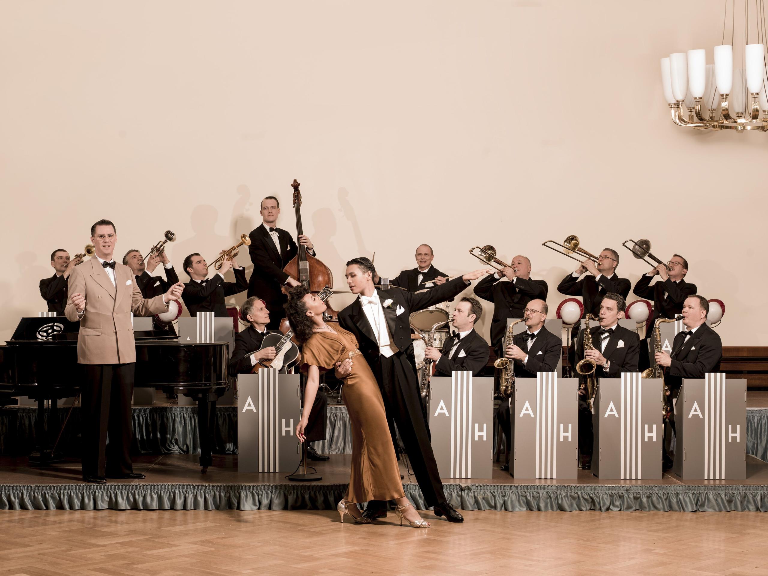 A dancing couple stands in an elegant pose in front of a big band.