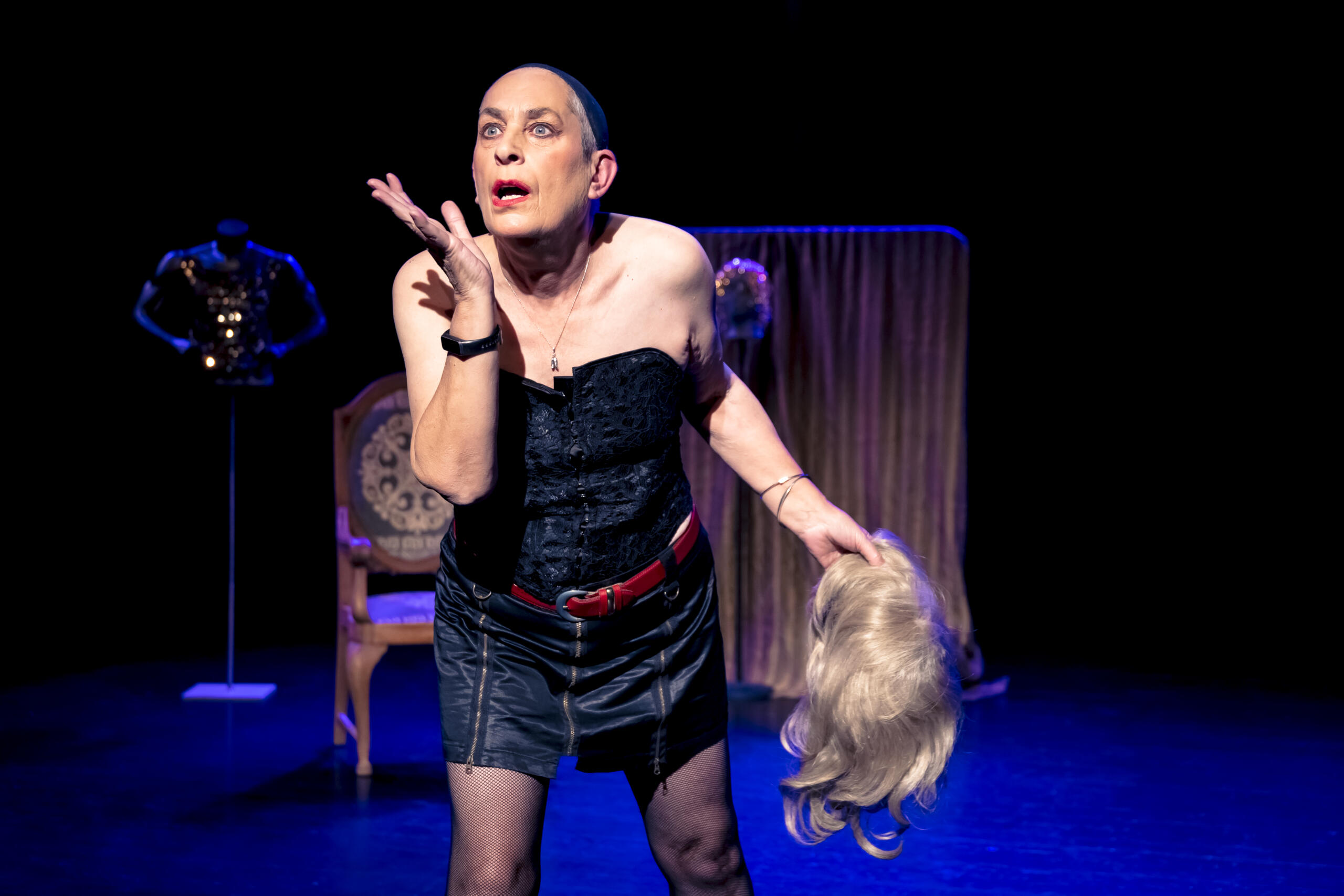 Claire Dowie on a stage with decoration in the background, a wig in her hand and a black dress