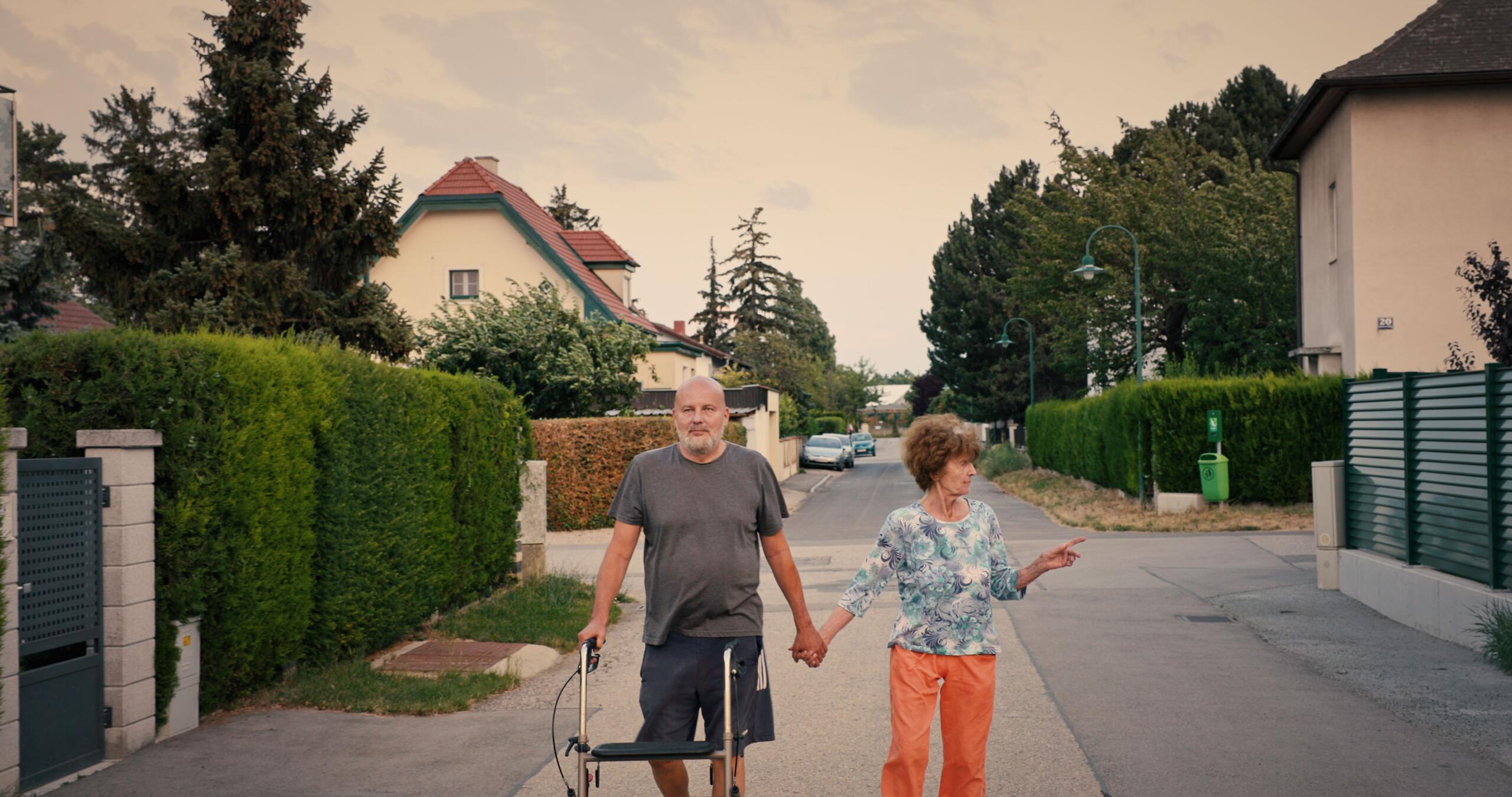 Ein mittelalter Mann und eine alte Frau gehen durch eine Wohnsiedlung.