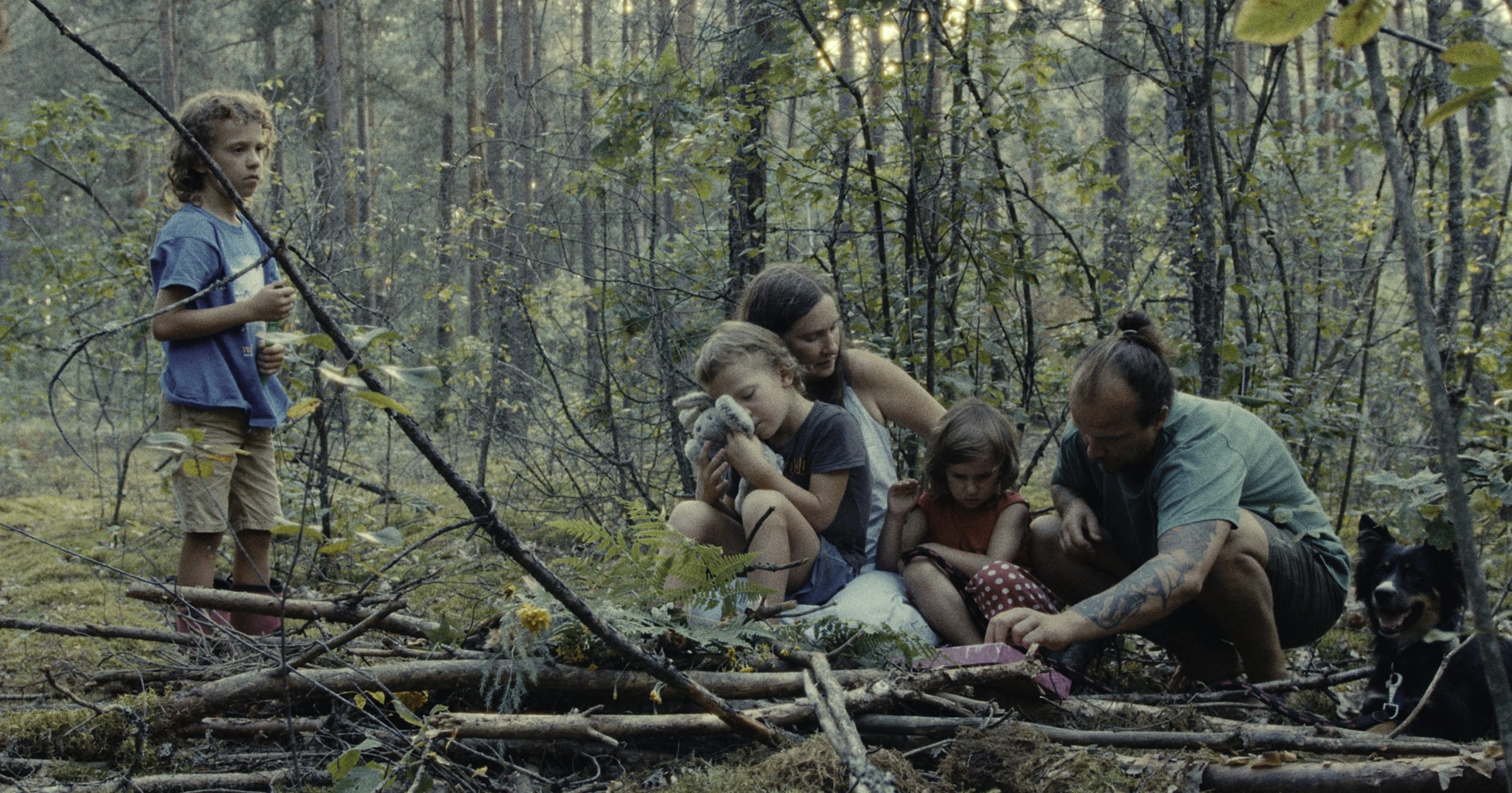 Eine Familie mit Vater, Mutter und drei Kindern sitzt in einem dichten Wald.