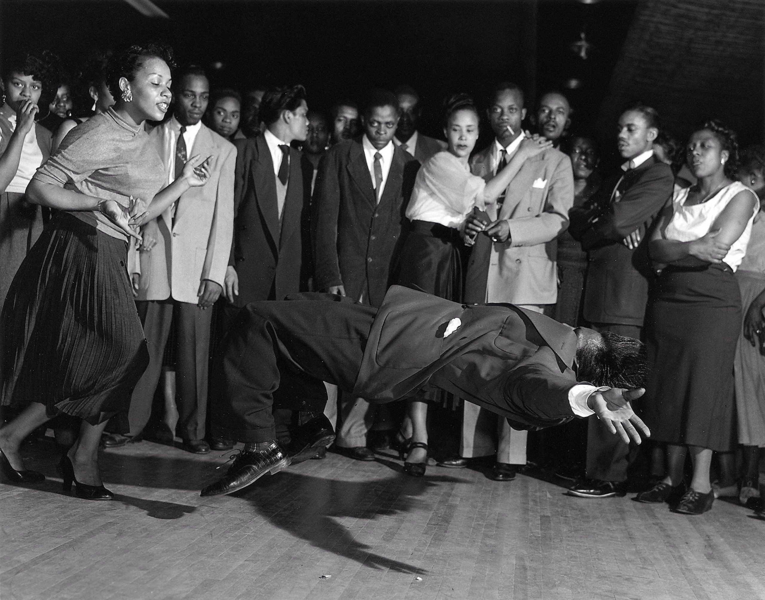 Eine schwarz-weiß Aufnahme von einem Dancebattle. Eine Menge steht staunend um einen tanzenden Mann.