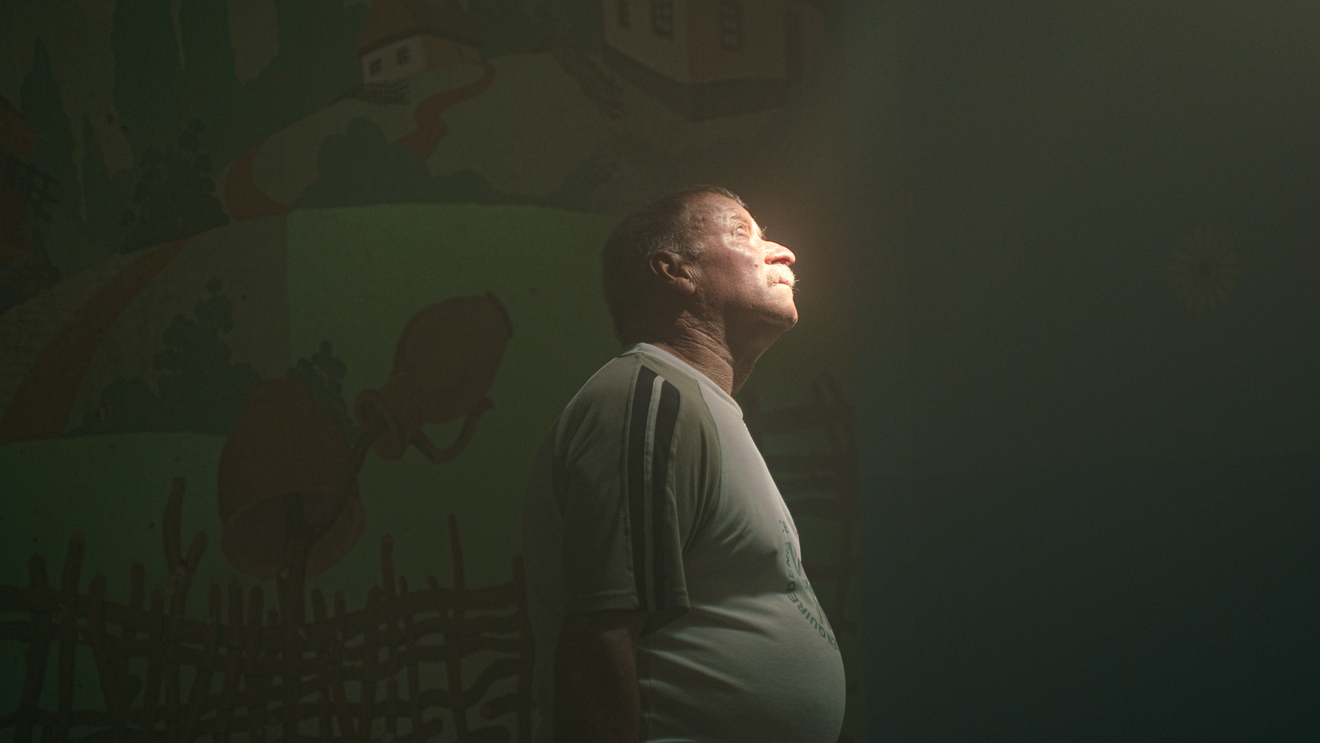 Ein Mann steht in in einem dunklen Keller und hält sein Gesicht unter das Licht eines Kellerfensters.