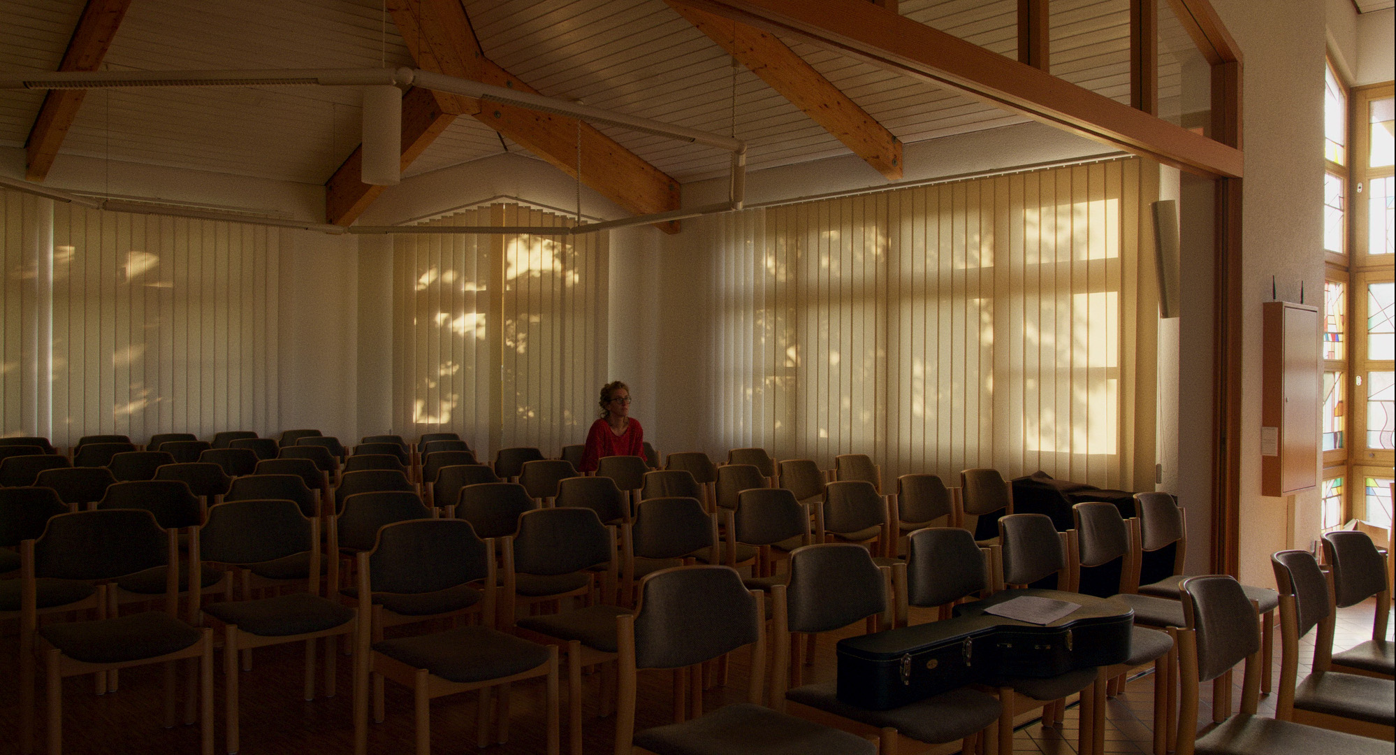 A woman sits in a dark and empty parish hall.