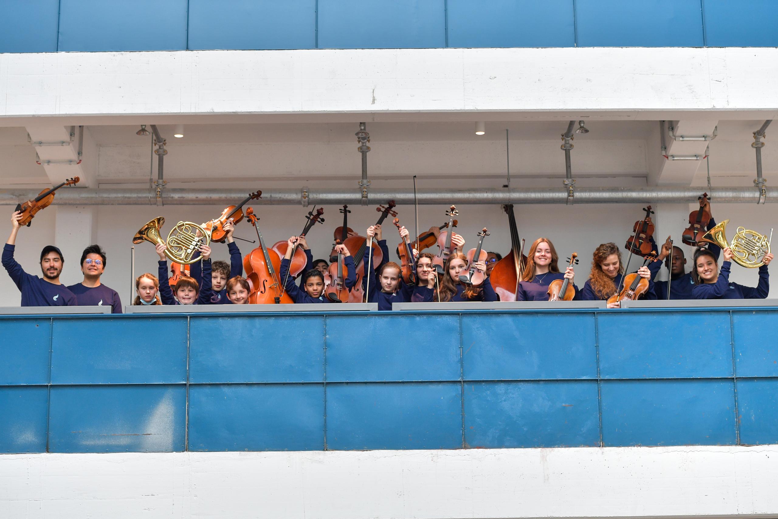 Kinder stehen auf den blauen Balkonen der Halle E und halten ihre Musikintrumente in die Luft.