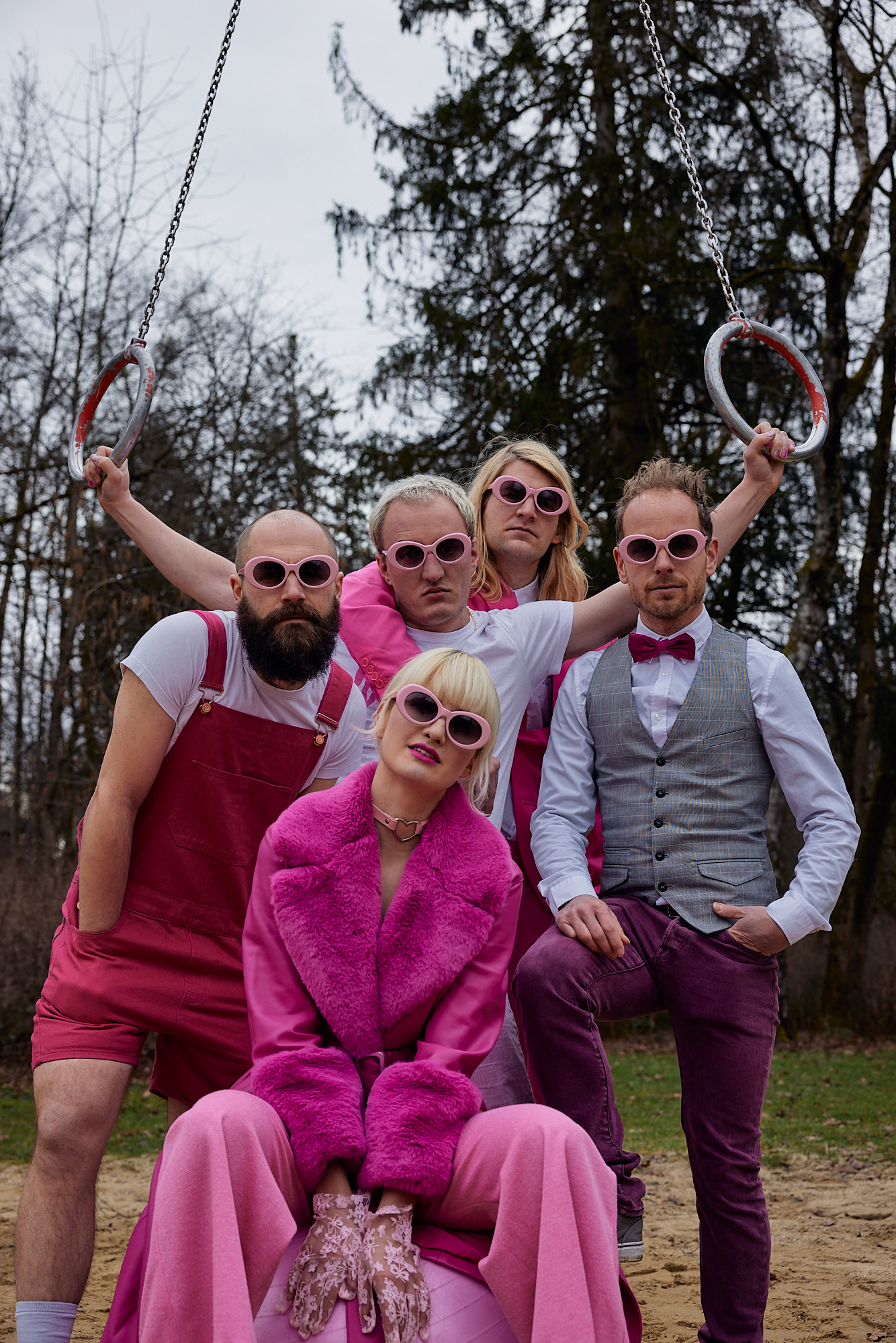 Four men and a woman on a playground in nature. They wear pink sunglasses.