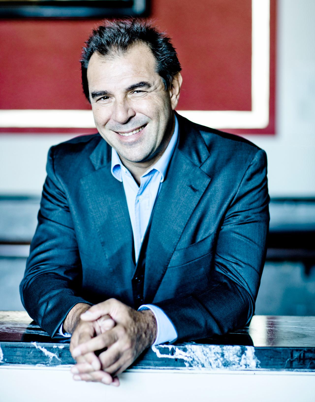Conductor Daniele Gatti leans with his arms on a counter and laughs into the camera