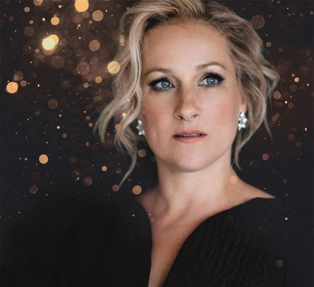 Portrait shot of soprano Diana Damrau against a dark background with gold colored light dots