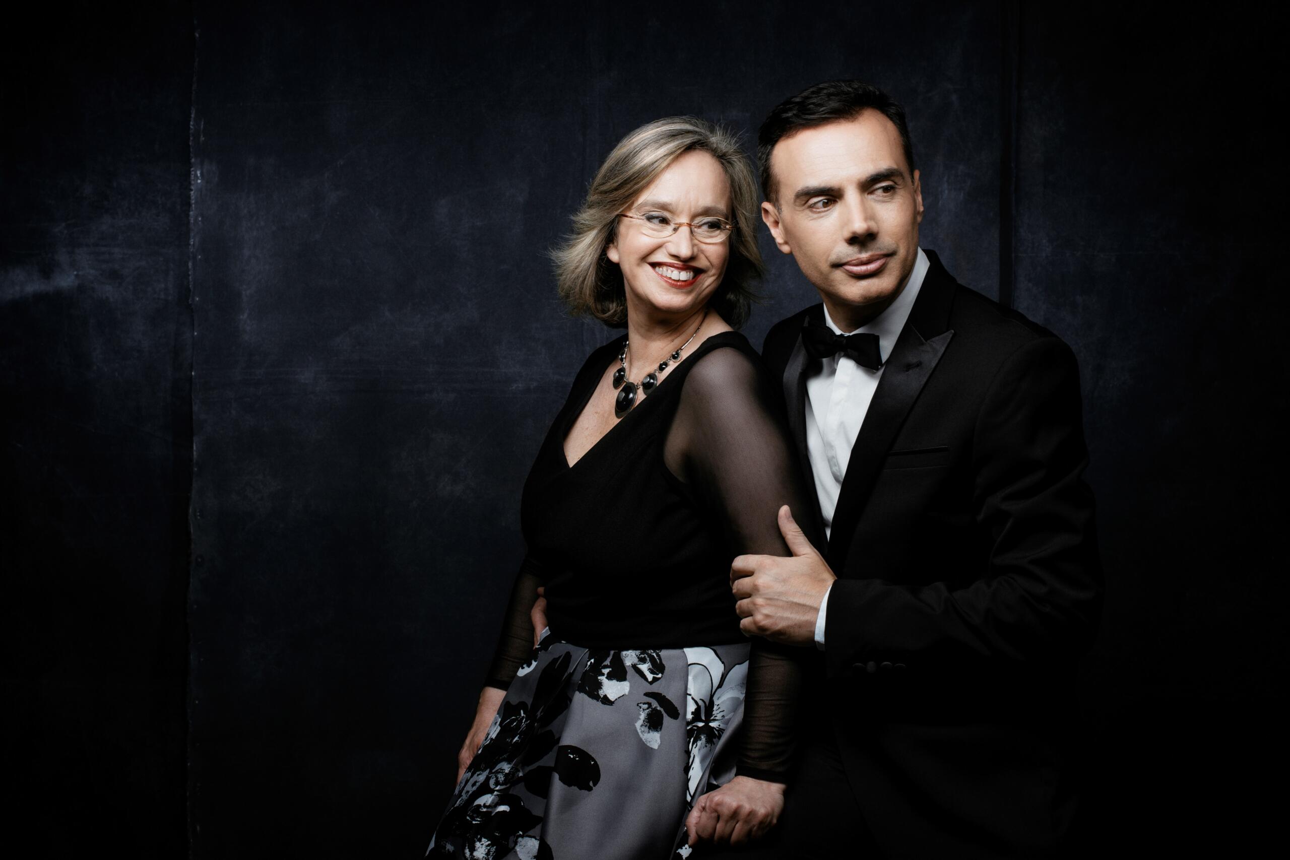 A dark background with a woman and a man in evening dress in front of it.