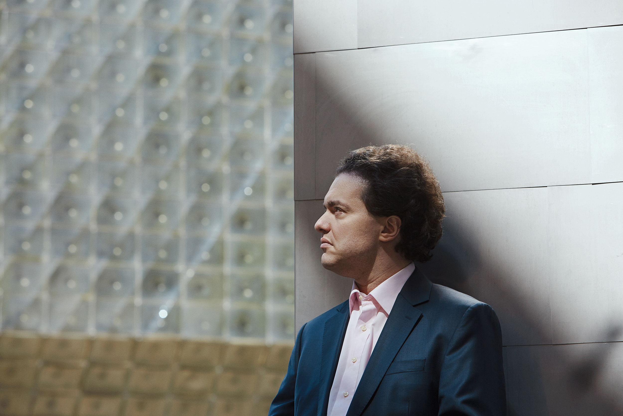 Profile shot of pianist Evgeny Kissin. He leans against a gray wall and looks to the left.