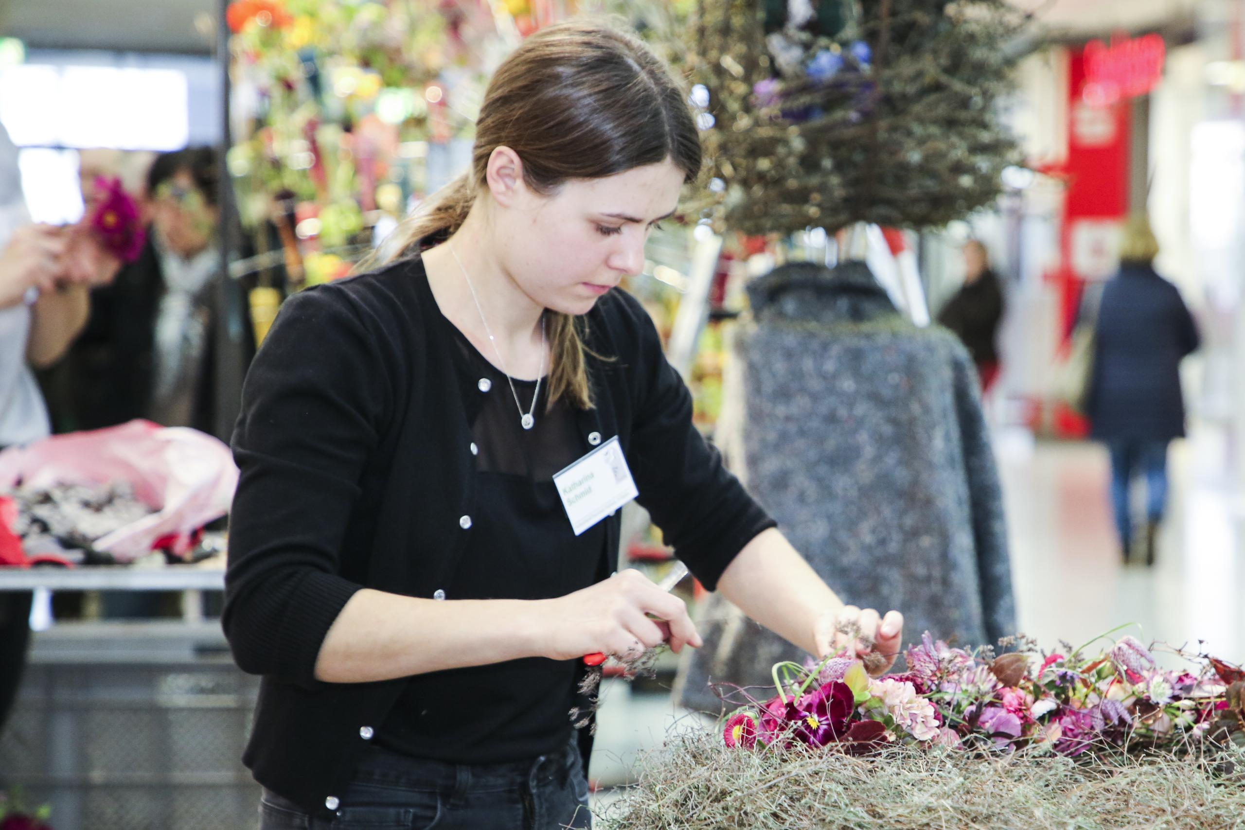 A florist is making her floral work. She ties pink flowers and bushes into a wreath.