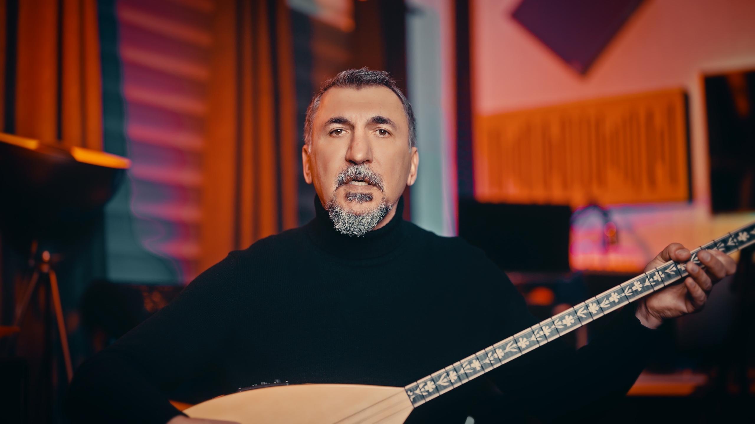 The musician Ferhat Tunç looks head-on into the camera, he plays a stringed instrument and sings. In the background you can guess a sound studio.
