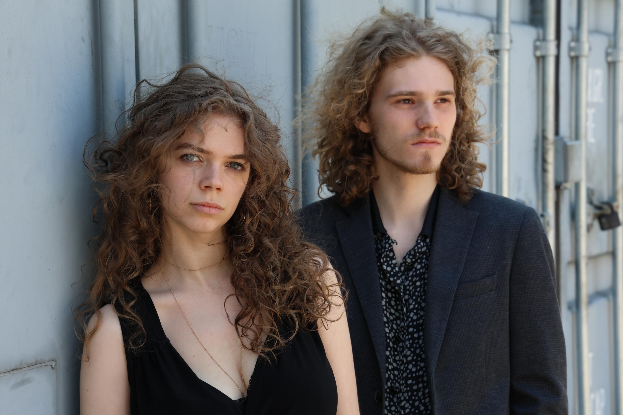 A young woman with wild curls and a young man stand in front of a metal container.