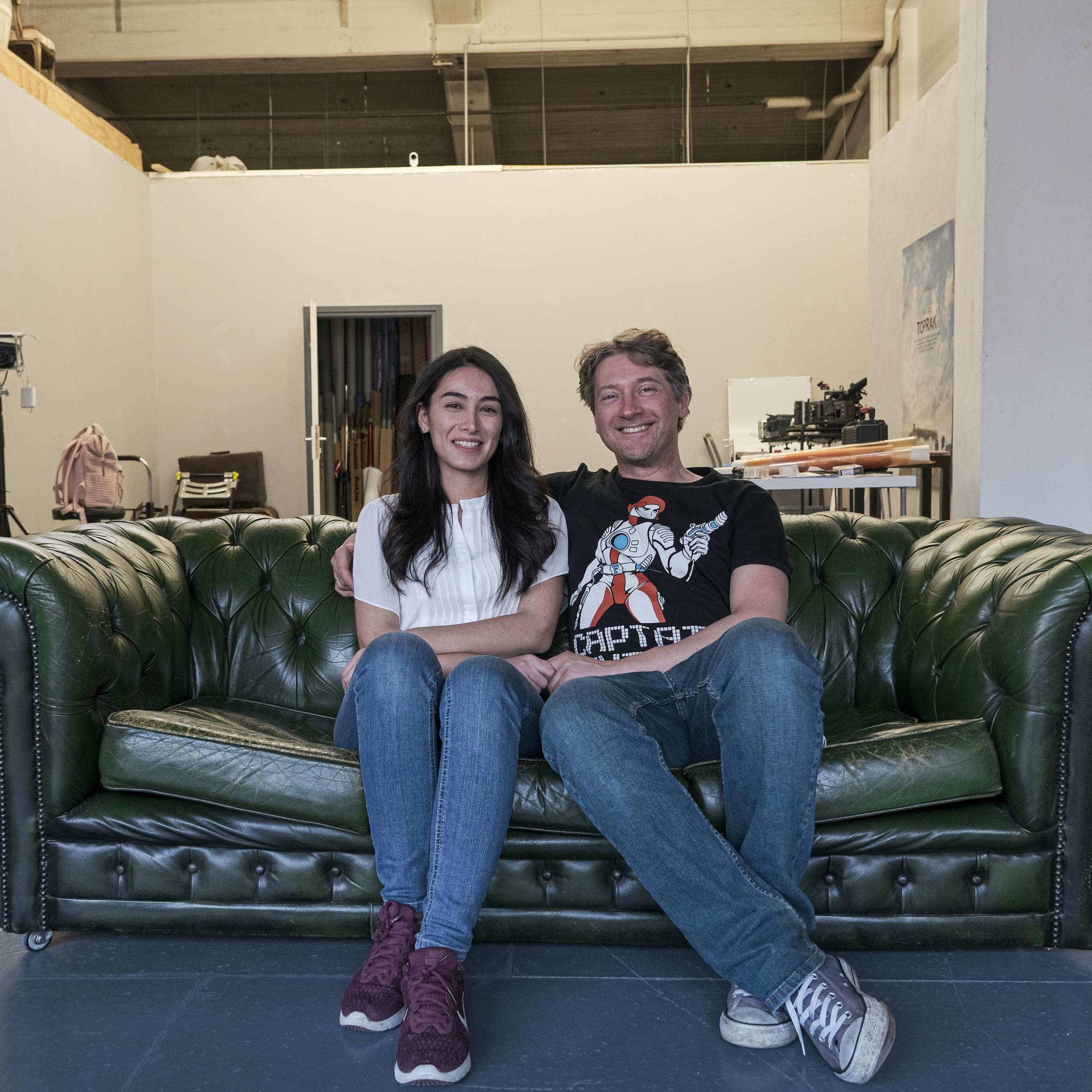 Filmmakers Sevgi and Chris Hirschhäuser sitting on a couch.
