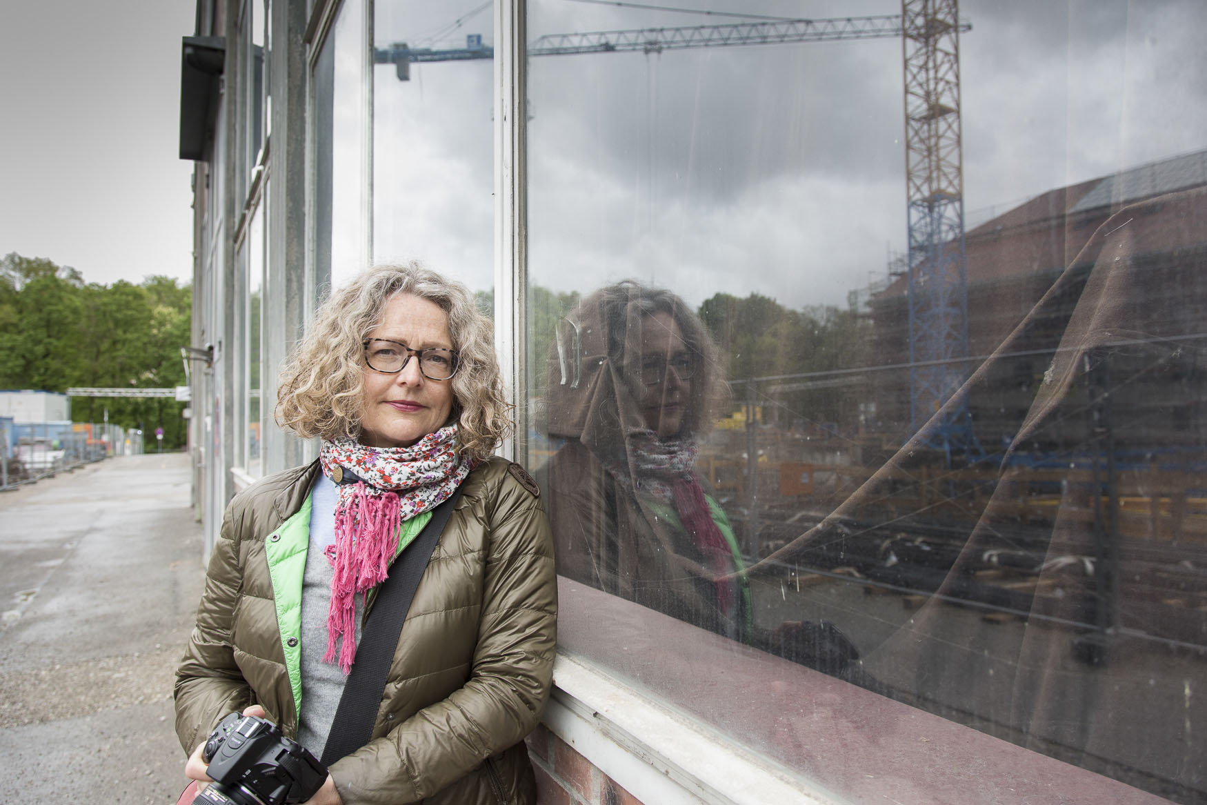 Amateur-Fotografin Jacqueline Tebcharani steht vor einem Fenster, in dessen Scheibe sich die Baustelle des entstehenden Gasteig HP8 spiegelt