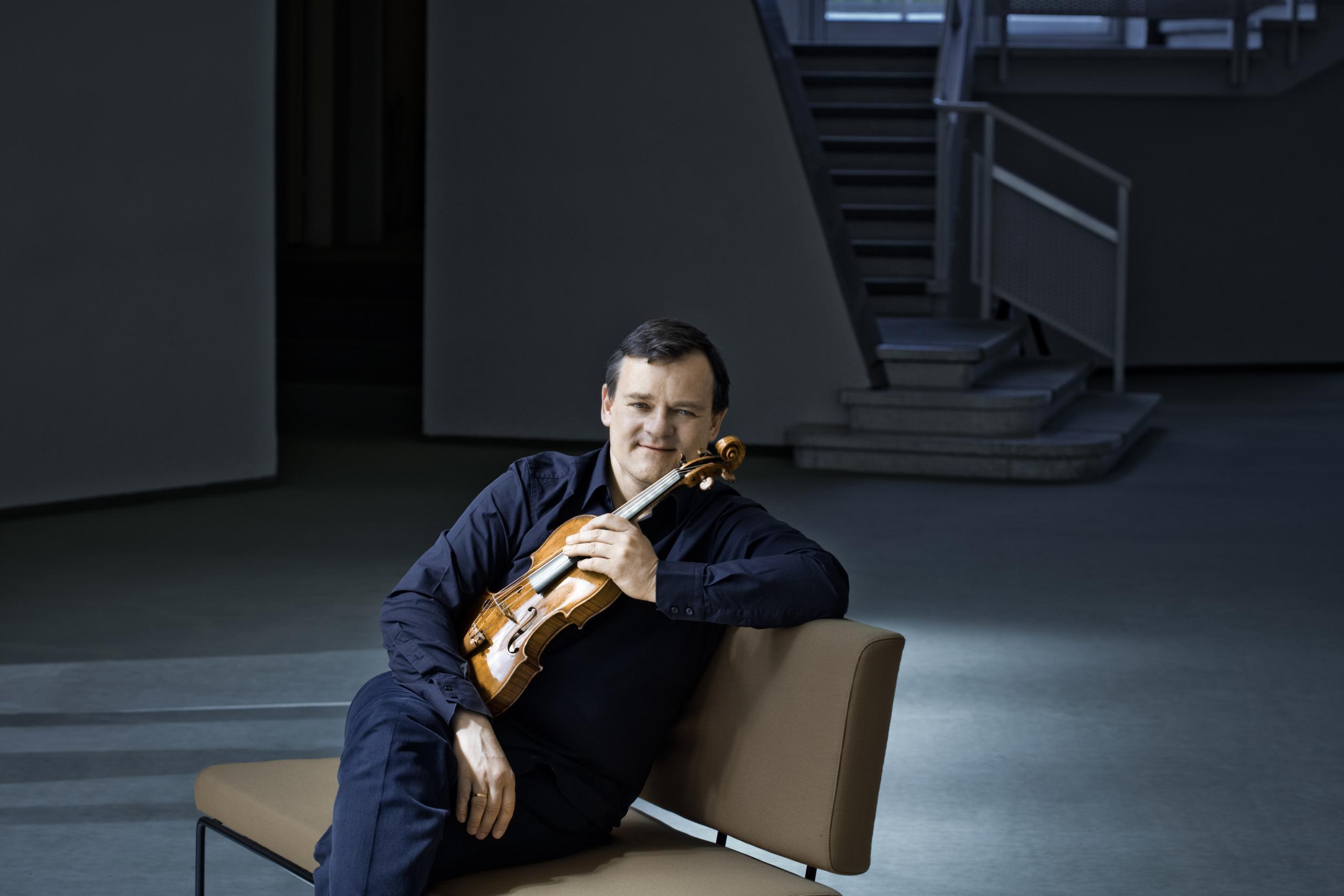 Frank Peter Zimmermann sitzt auf einem Sofa und hält die Geige in der Hand