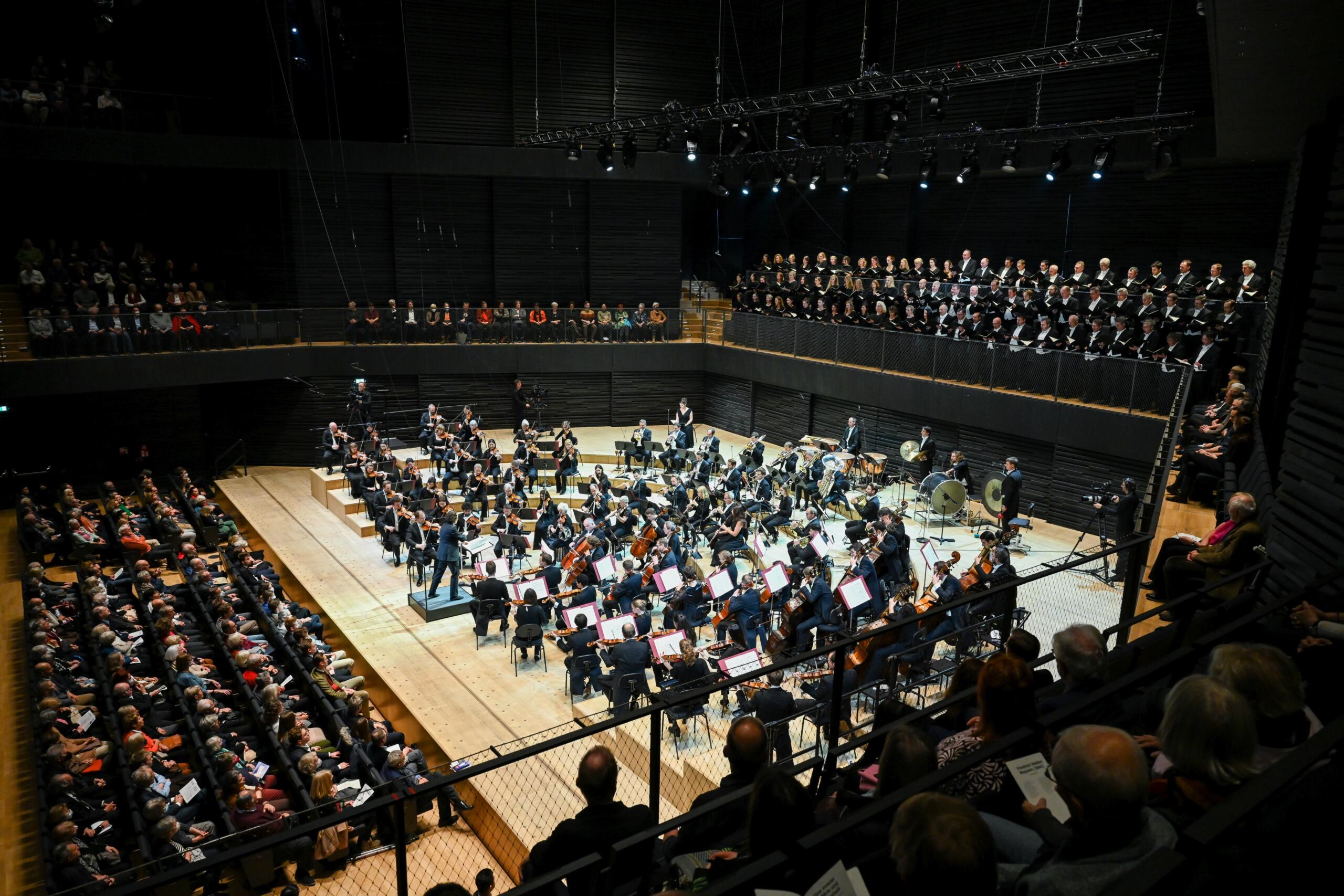 The Munich Philharmonic Orchestra sits on the stage of the Isarphilharmonie.
