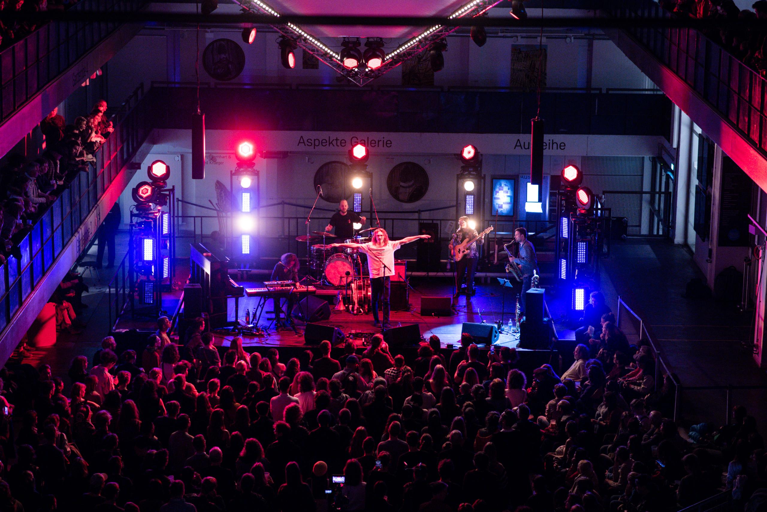 View from above in Hall E of the stage, which is lit up in red and blue. Singer Florian Paul stands there with his arms outstretched.