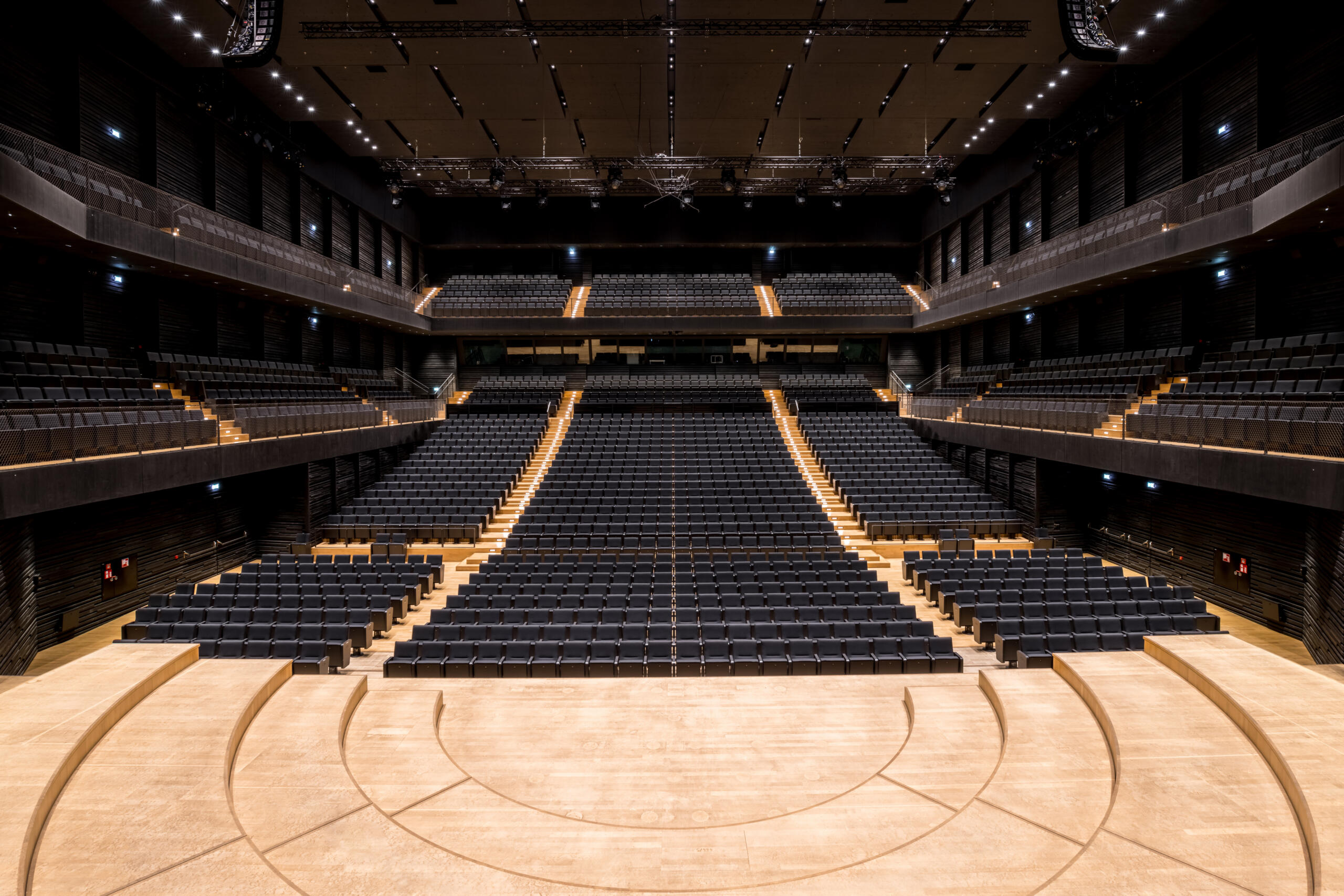 Blick in den dunklen, symmetrischen Zuschauerraum des Konzertsaals mit Parkett, Balkonen und Rängen, von der hellen Bühne aus.