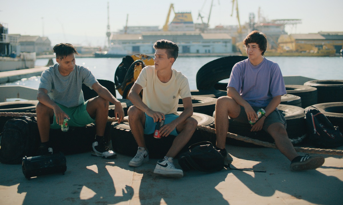 Three teenagers sit on car tires in a port area.
