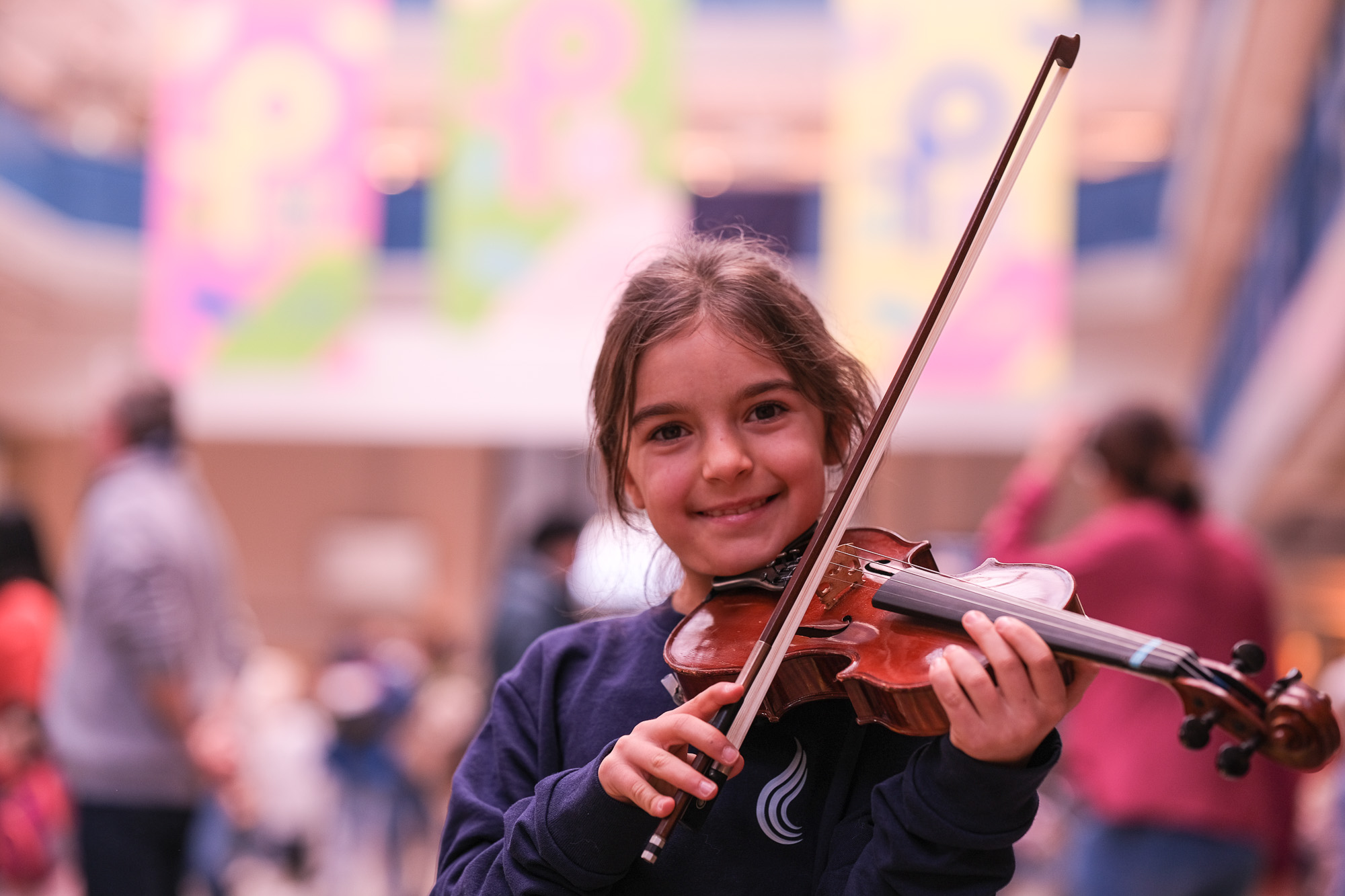 A girl from the social music project C.O.N.SONANZA looks into the camera with her violin, smiling. The violin bow is ready.
