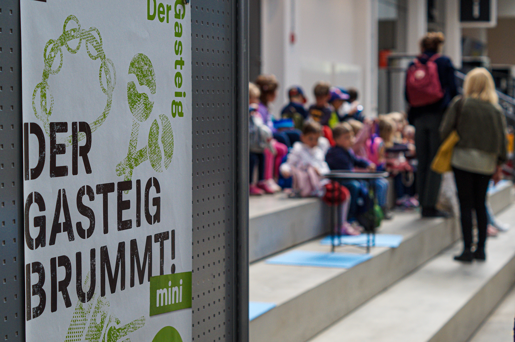 Children wait in Hall E next to the poster for "Der Gasteig brummt!"