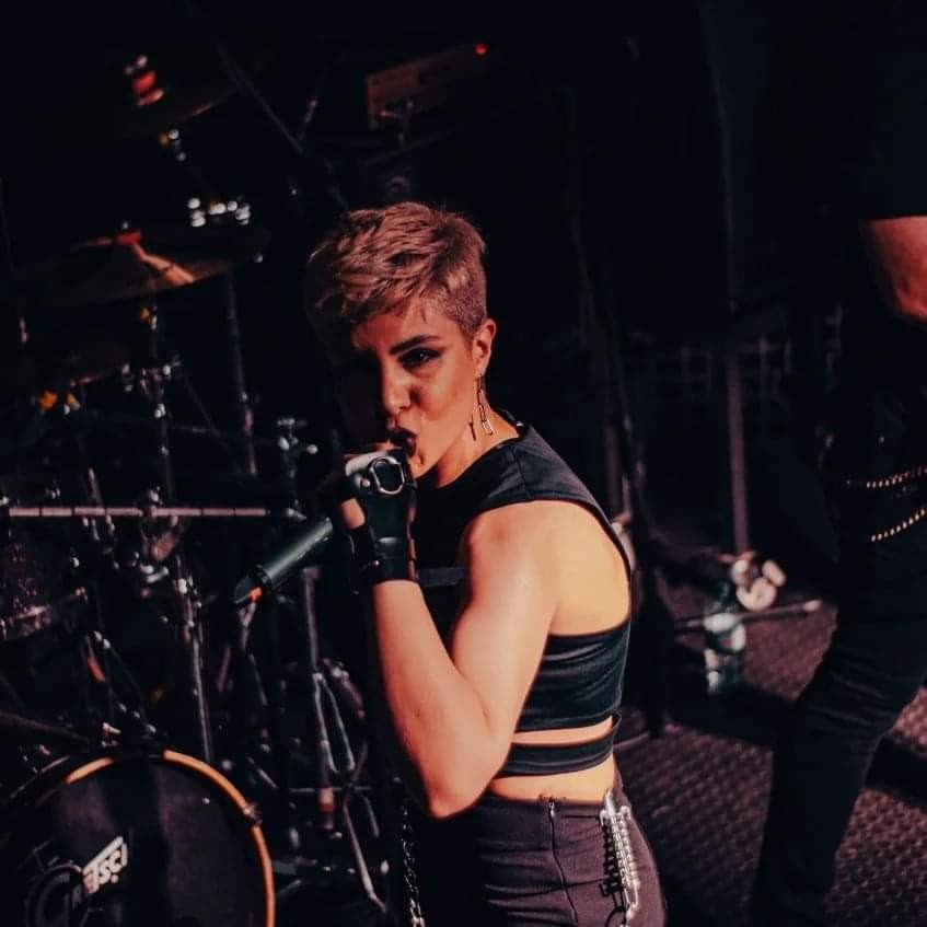 The singer Kian on the stage, in the background a drum kit, she sings into the mic.