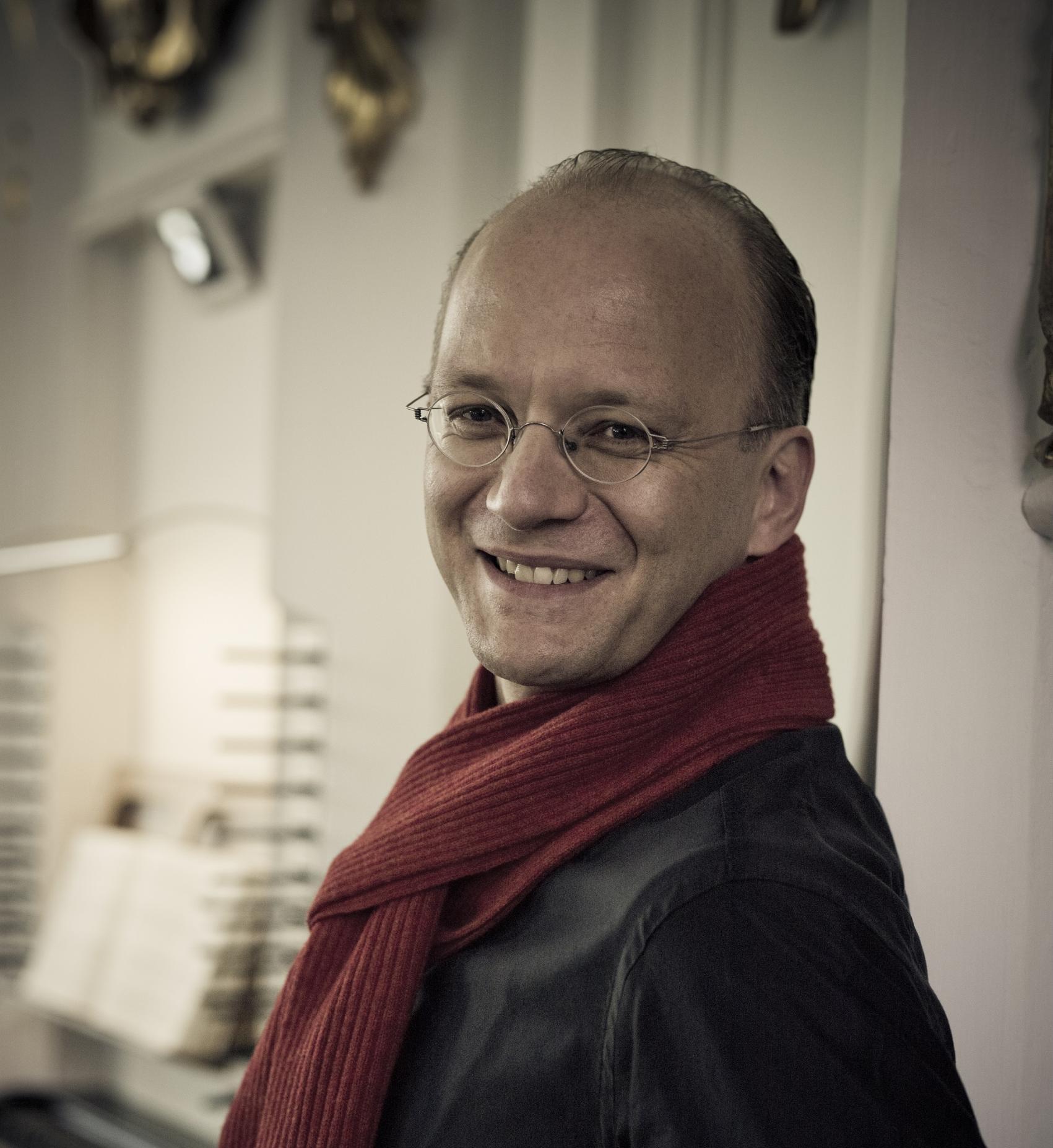Portraitaufnahme des Dirigenten Hansjörg Albrecht in schwarzem Hemd und mit rotem Schal.