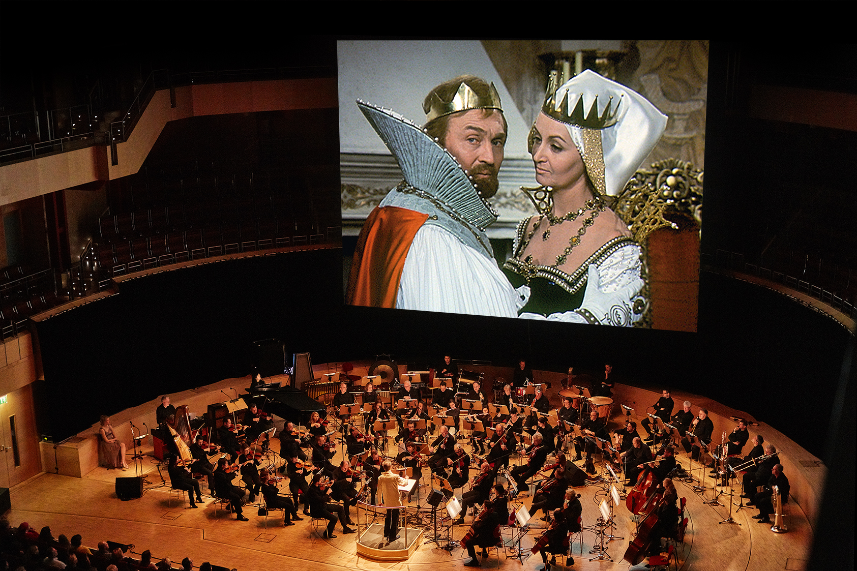 Eine Bühne mit dem Orchester, im Hintergrund eine Leinwand mit einer Filmszene mit König und Königin.