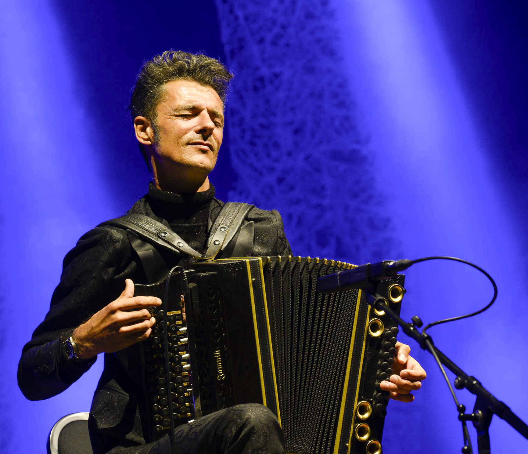 The musician Herbert Pixner with accordion on a stage. The background is blue.