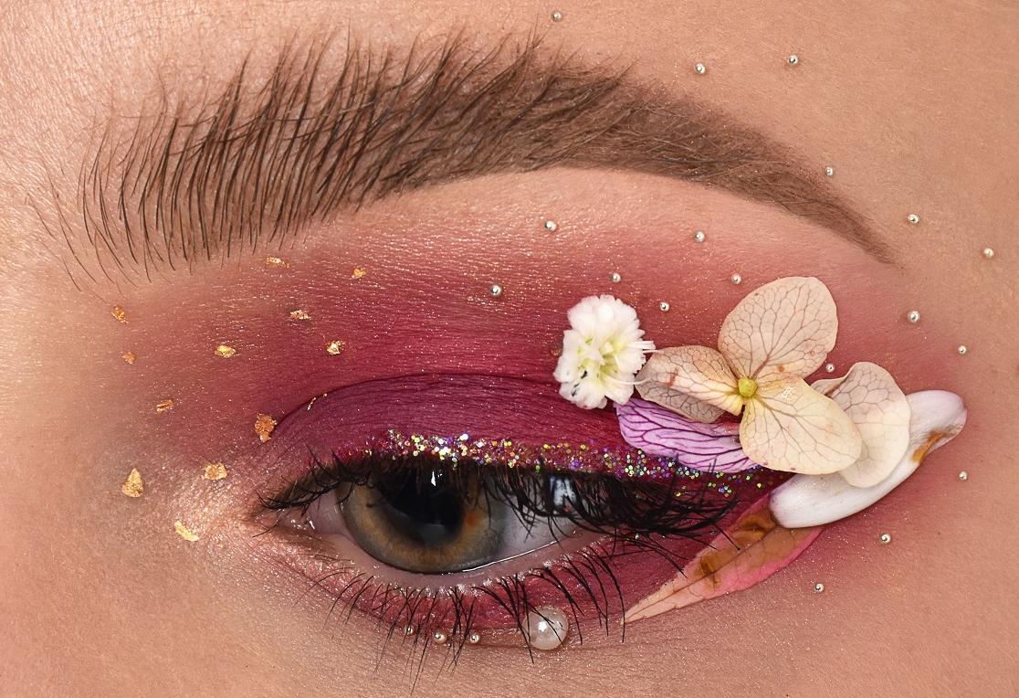 Nahaufnahme einer Augenpartie, aufwändig geschminkt mit aufgesetzen echten Blumen.