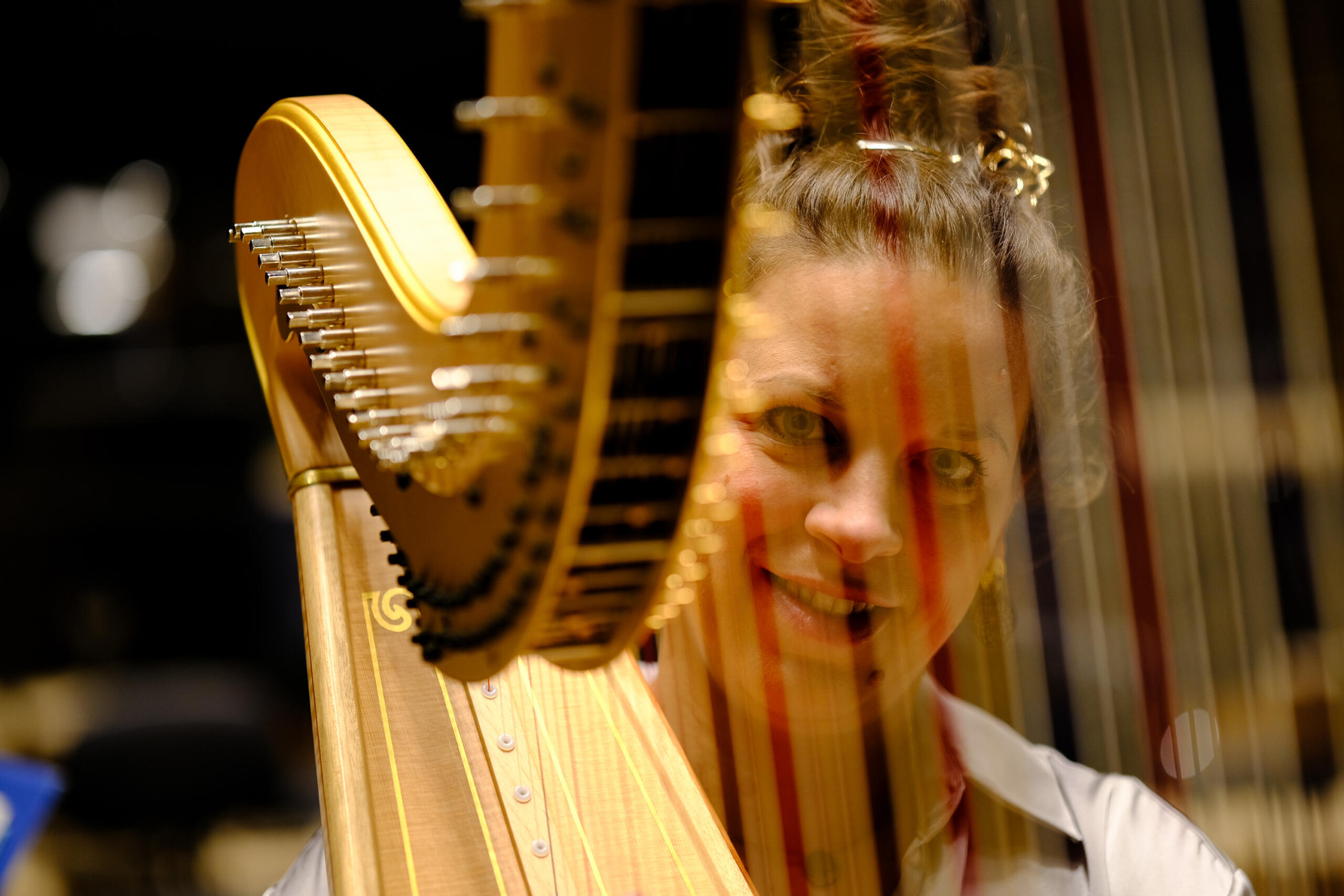 The harpist looks between the strings of her harp and smiles.