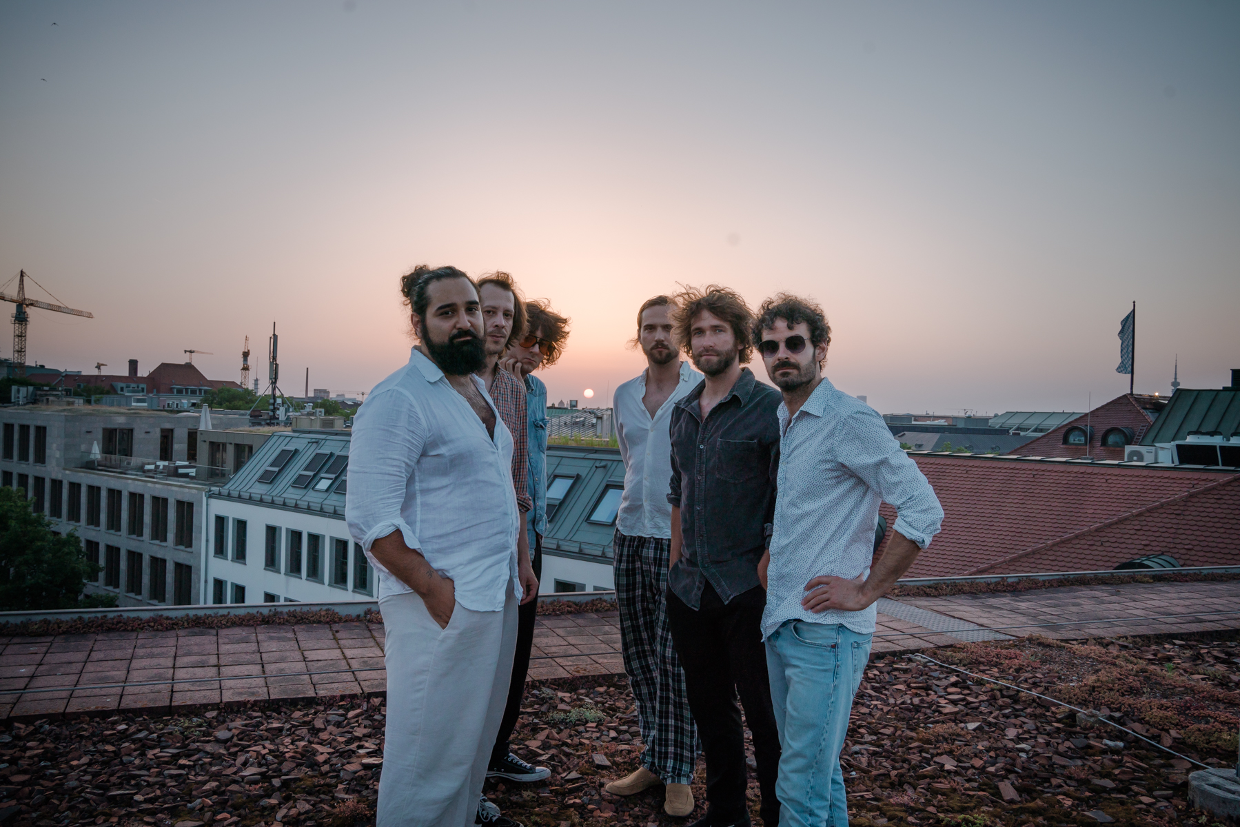 Sechs Männer stehen auf einem Flachdach, im Hintergrund sieht man die Silouette der Stadt München.