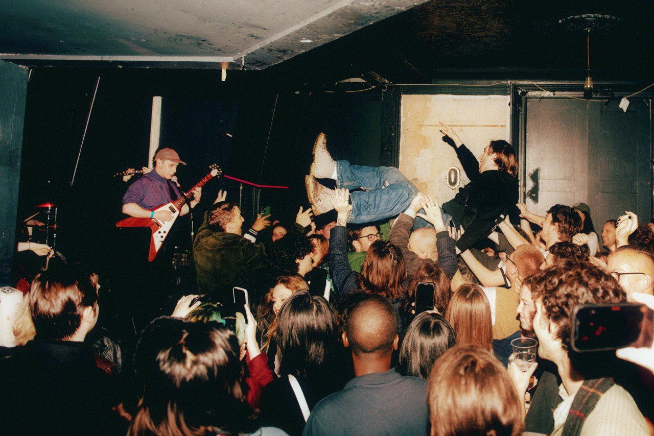 A small live club with audience, on stage a guitarist, the singer lets himself be carried by the crowd.
