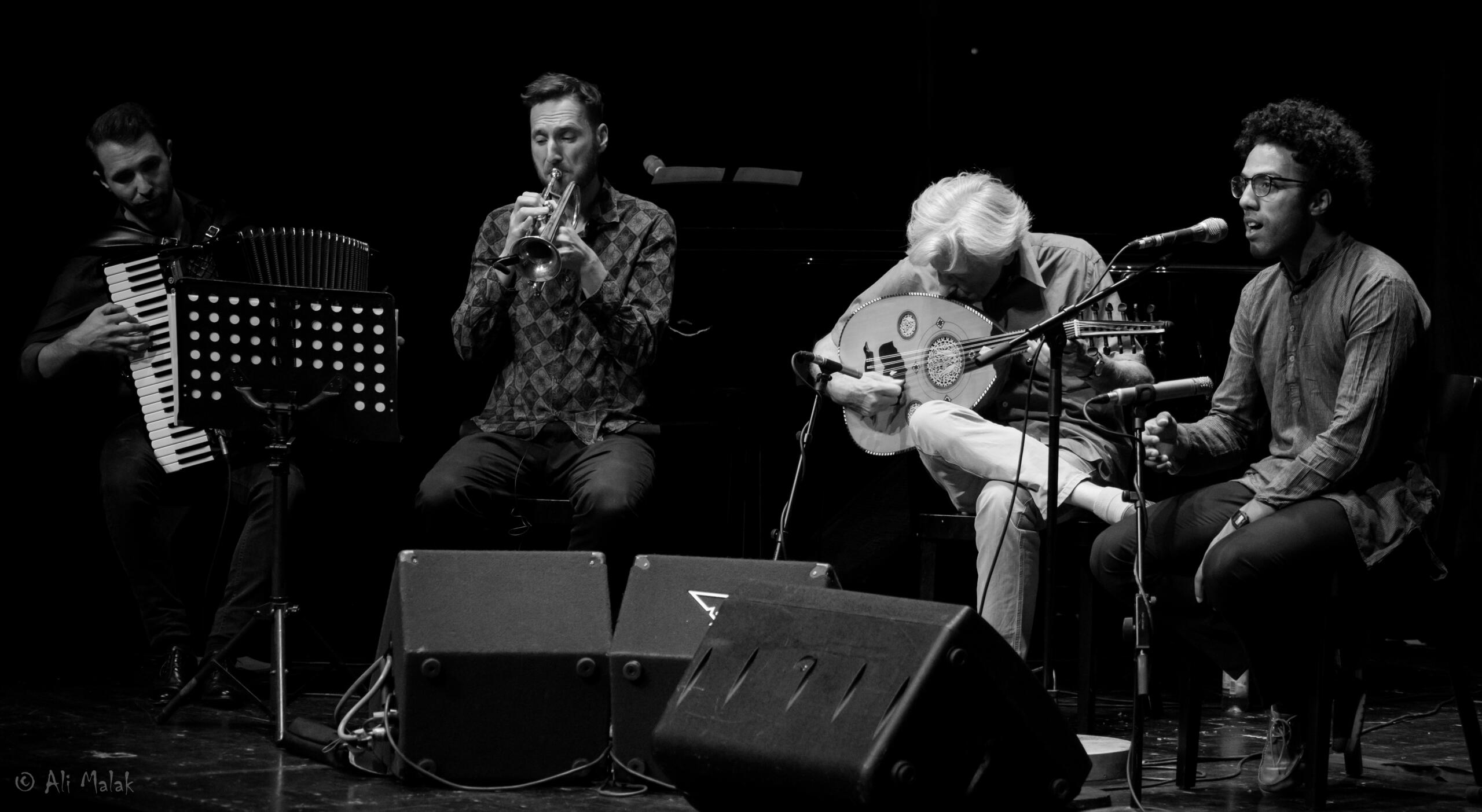 Four musicians sit side by side on a stage.