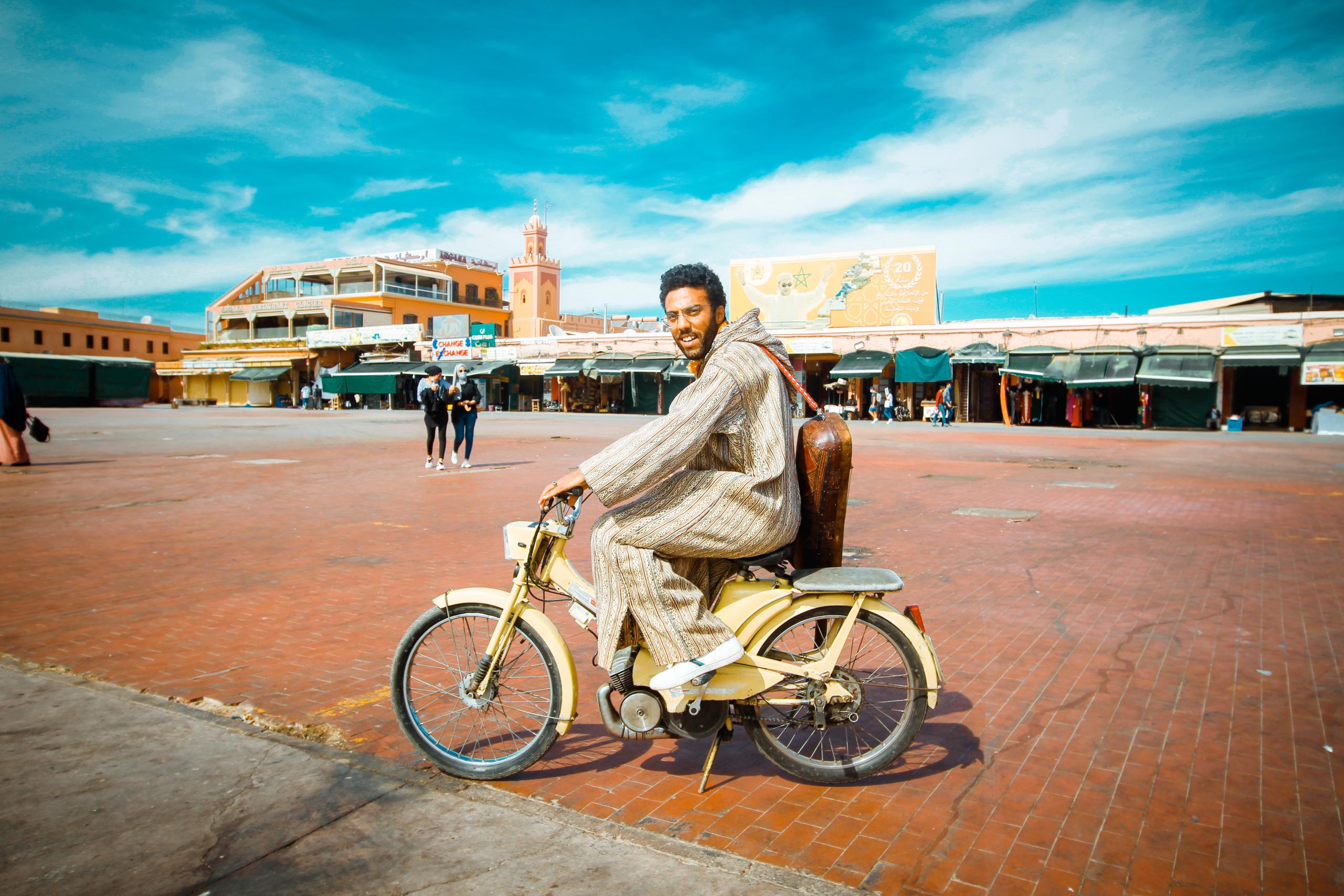 The musician Ramdan in a large marketplace. He is sitting on a moped in a traditional North African garb.