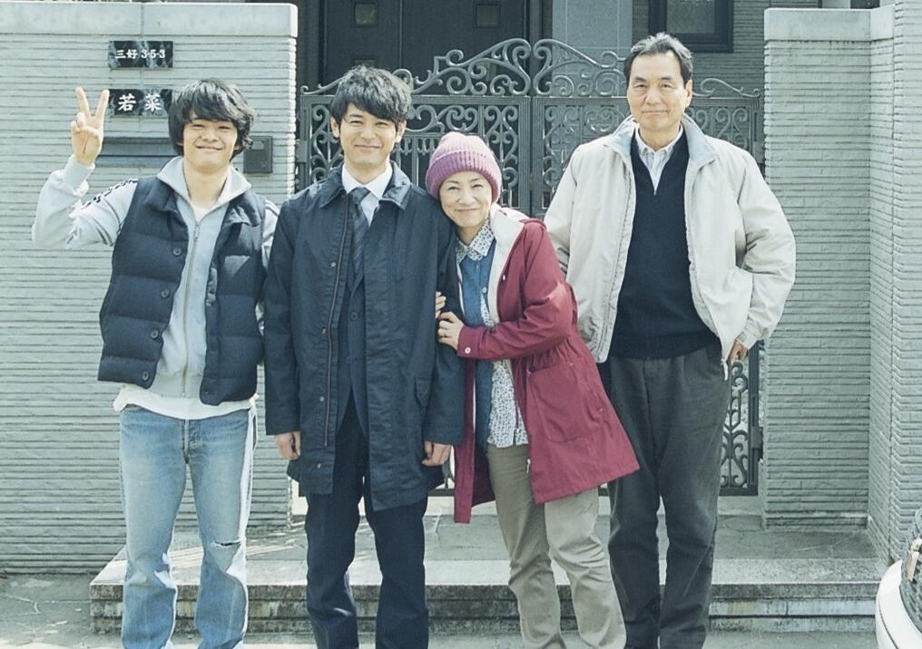 Eine vierköpfige Familie steht vor einem grauen Haustor und macht ein Familienfoto.
