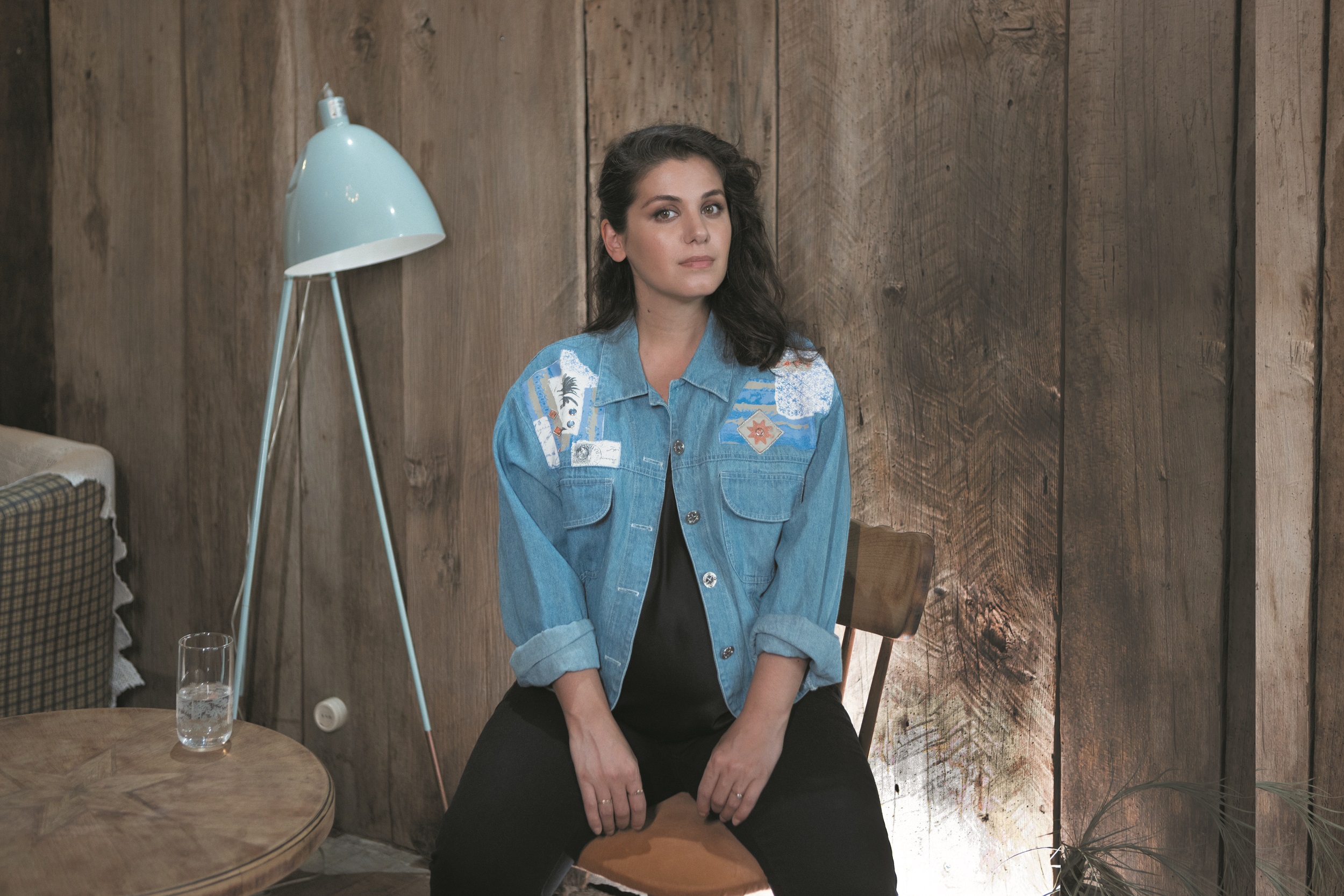 Katie Melua sits on a brown chair and wears a blue jeans jacket.