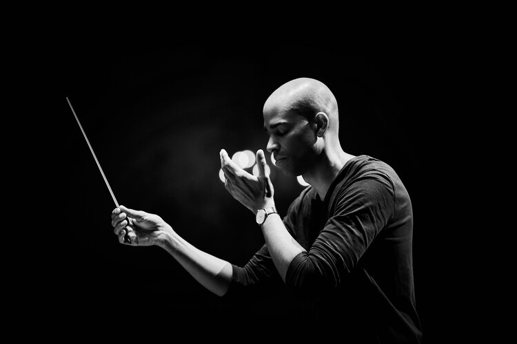 Black and white shot of conductor Edusei against dark background. He conducts with his eyes closed.